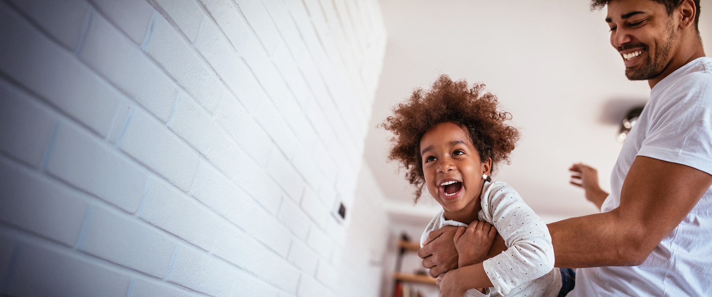 Photo of dad holding laughing daughter near a wall in the house.