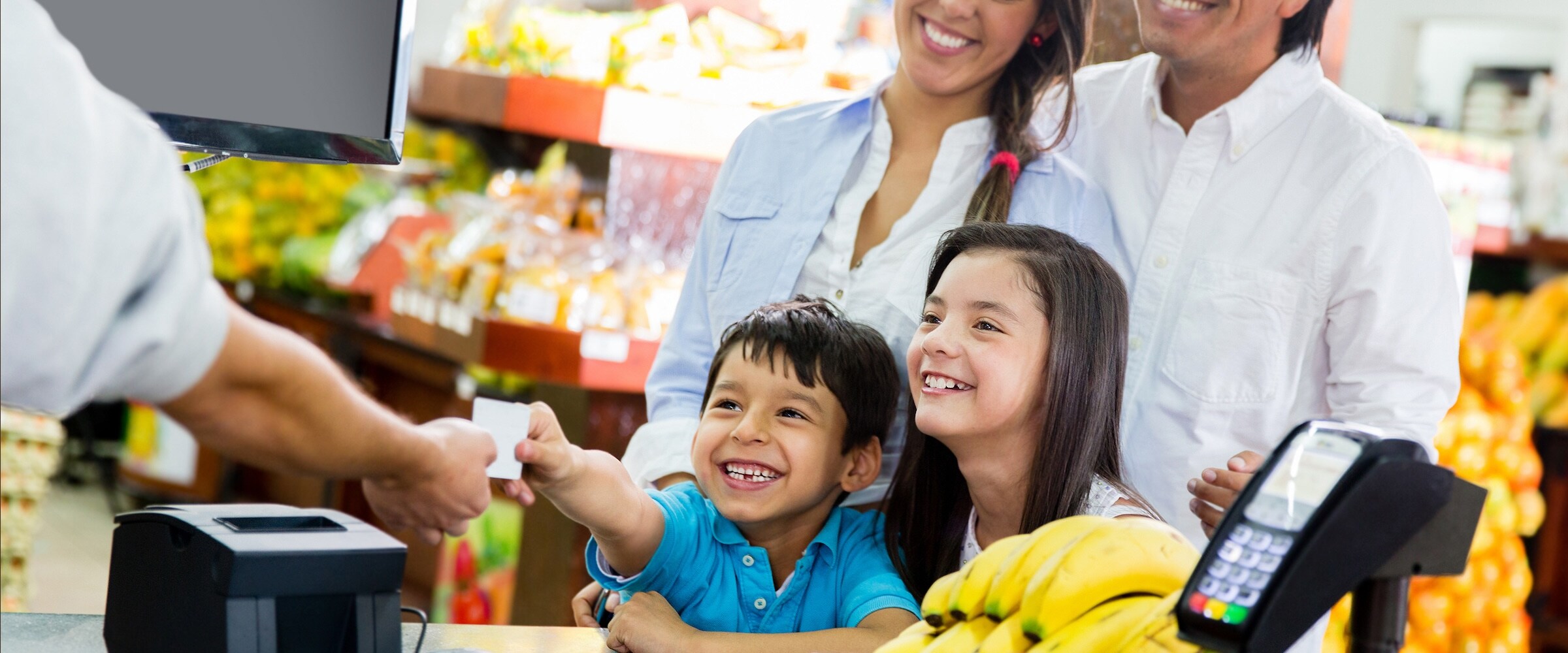 Photo of two kids with parents behind them paying for a store purchase with a credit card.