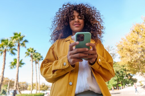 Young woman with curly hair using smartphone outdoors