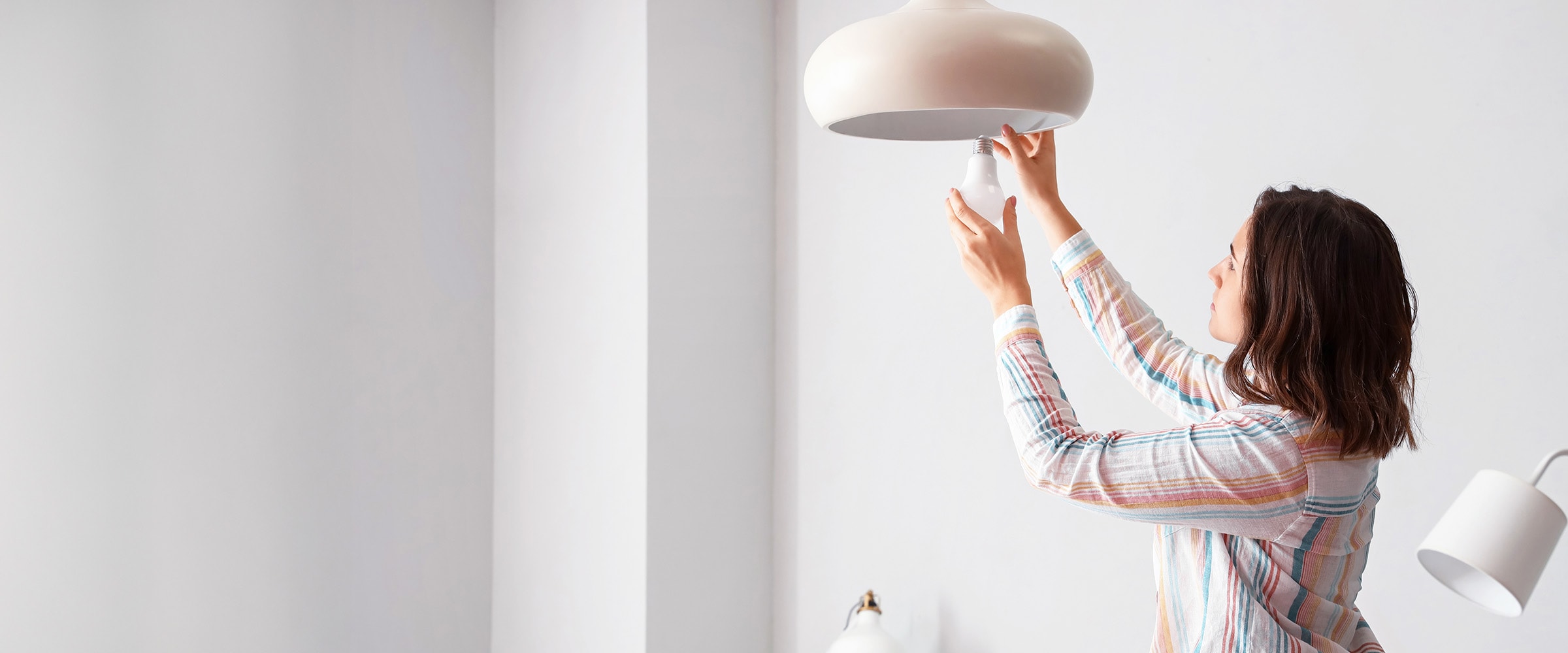 Photo of woman installing a light bulb in a ceiling lamp.