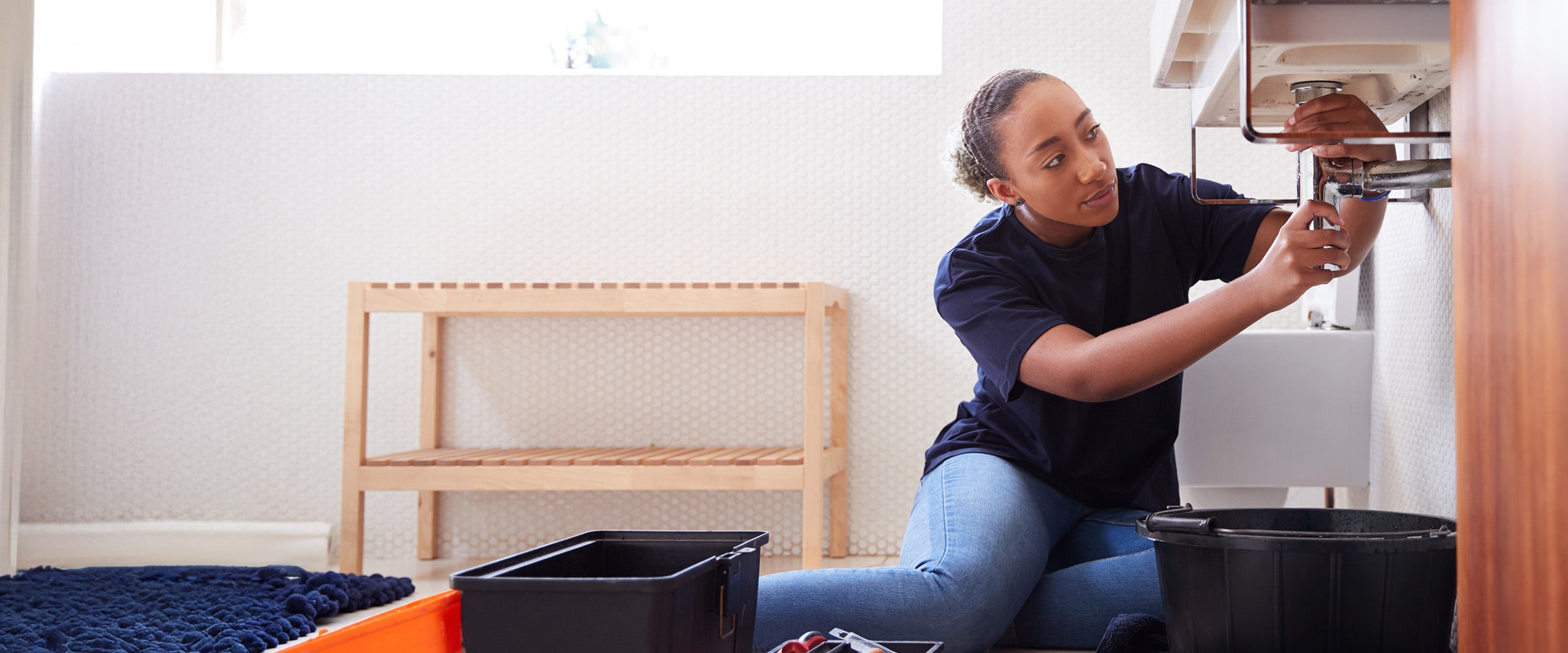 Photo of a woman fixing a pipe under her sink.