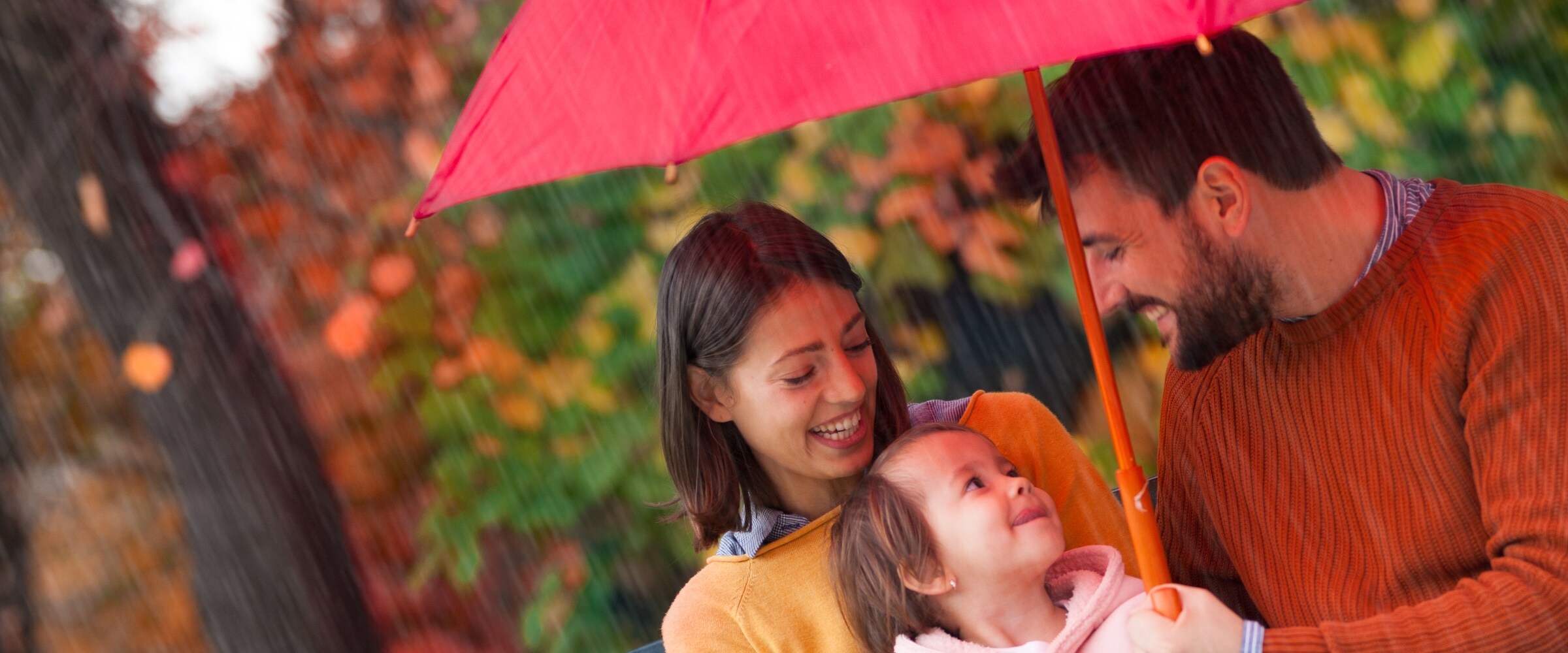 Photo of family under a red umbrella in the rain.