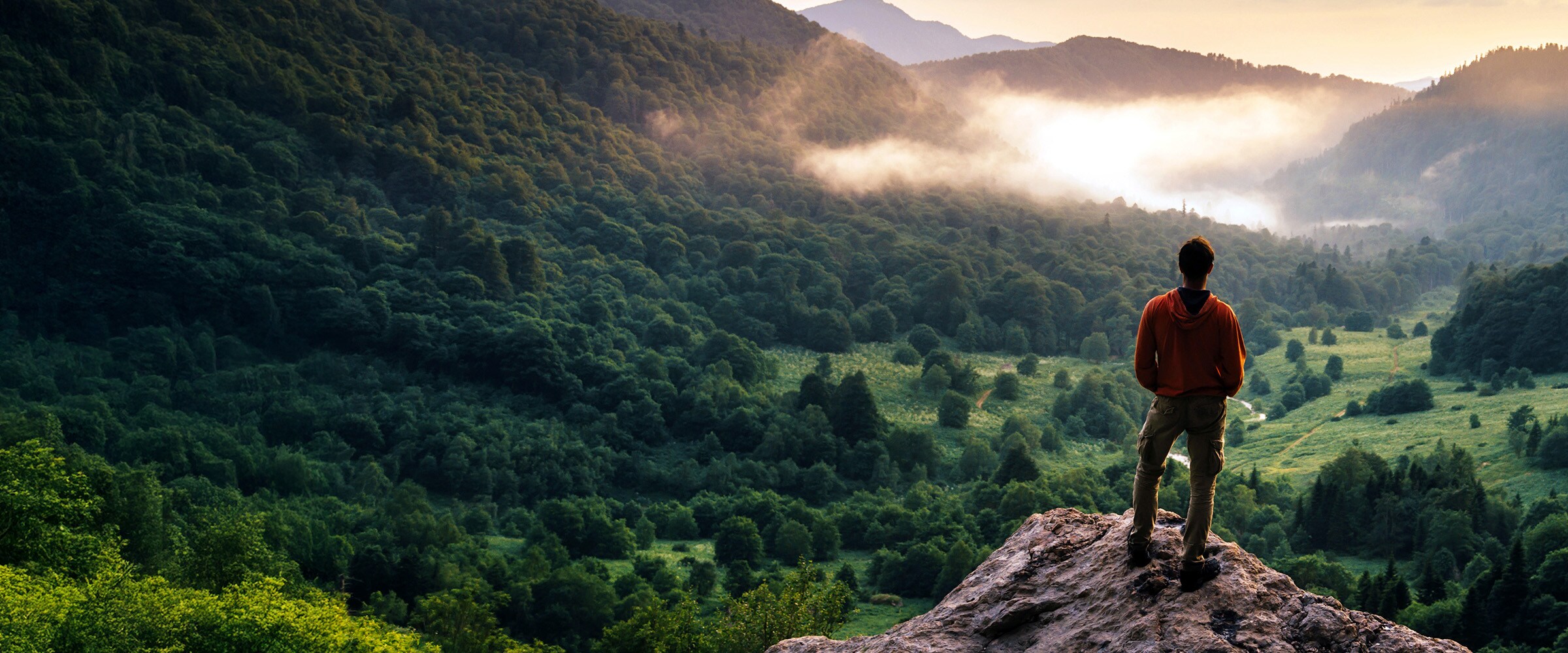 Photo of woman on top of mountain looking down at valley.
