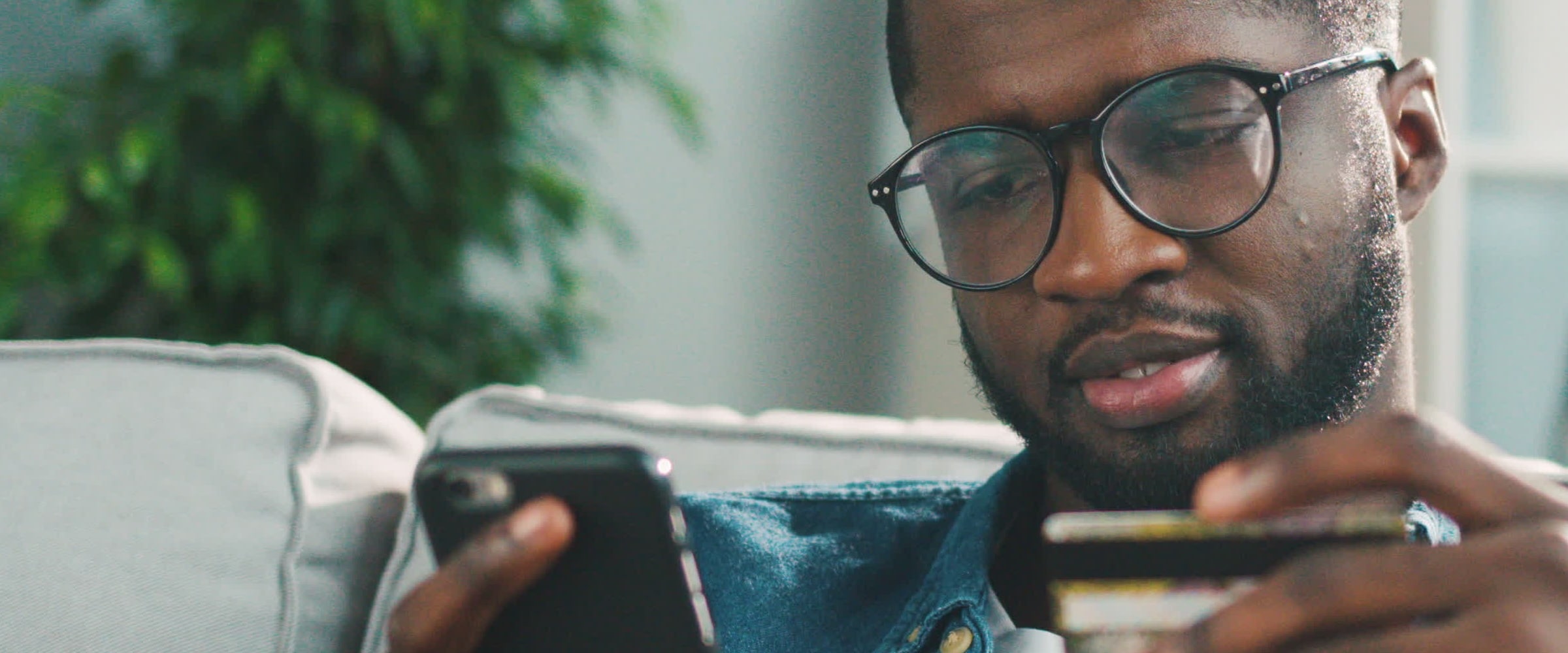 Close up photo of African American man looking at smartphone and credit card.