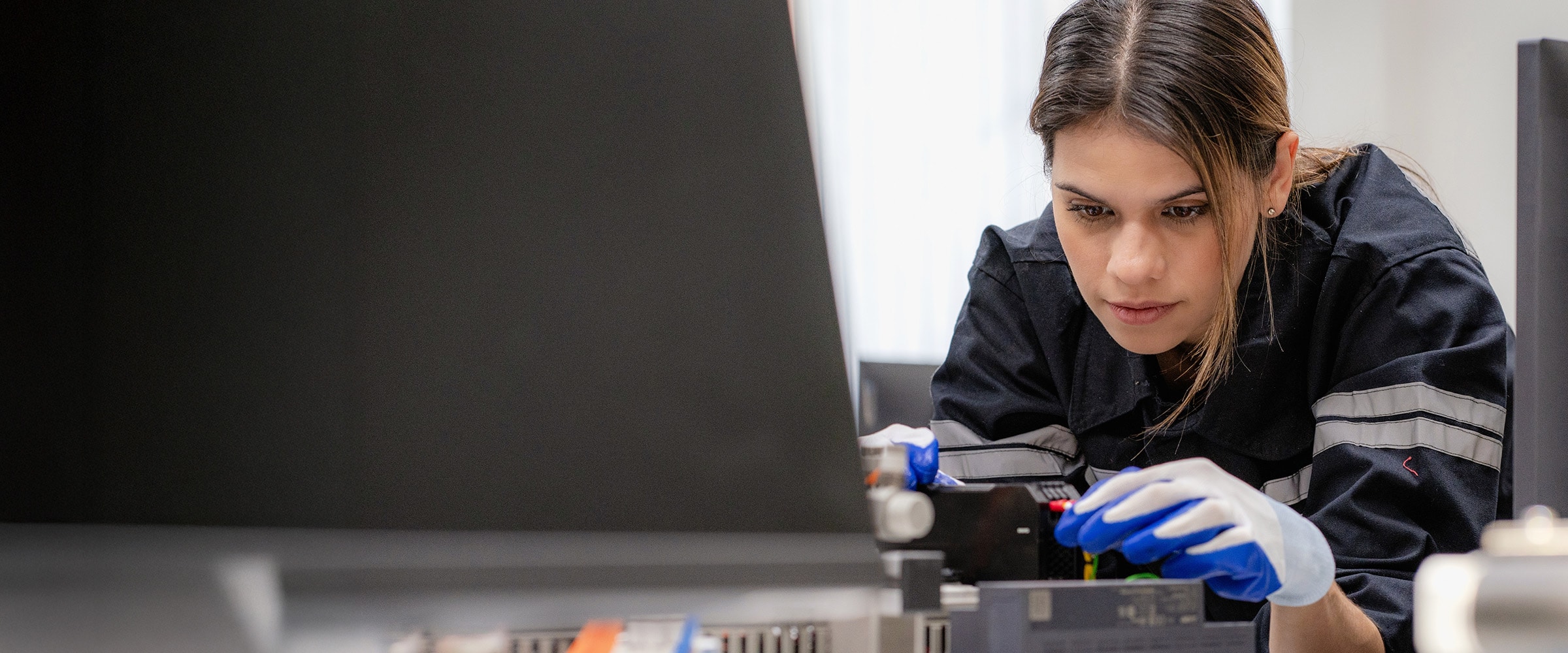 Photo of young woman in manufacturing jumpsuit working on a machine.
