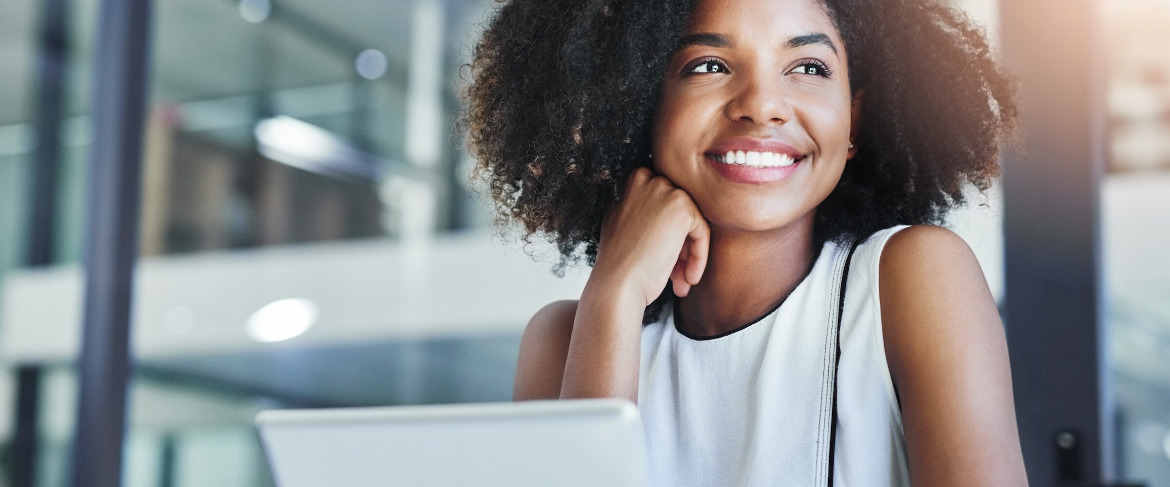 Photo of an African-american woman at laptop and looking out the window.