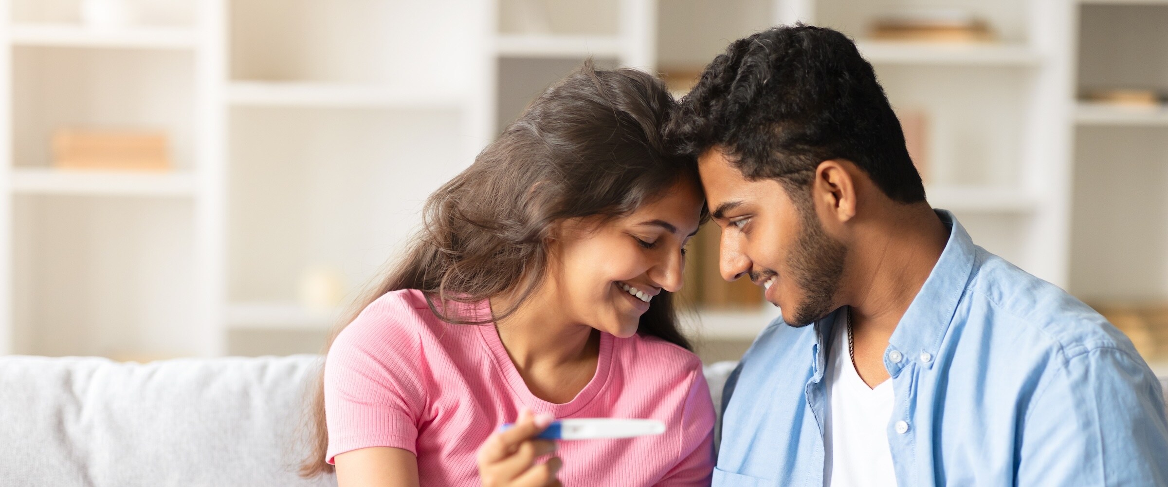 Photo of couple looking and smiling over a pregnancy test.