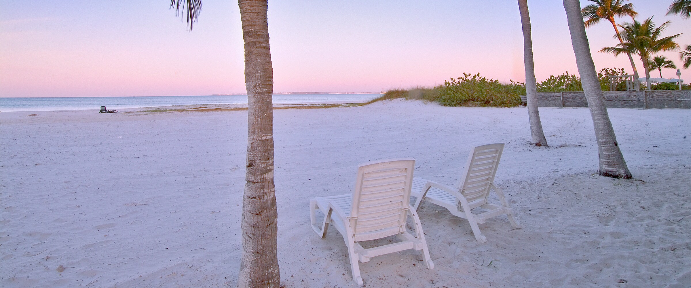 Image of a couple of beach chairs on a sunrise beach.