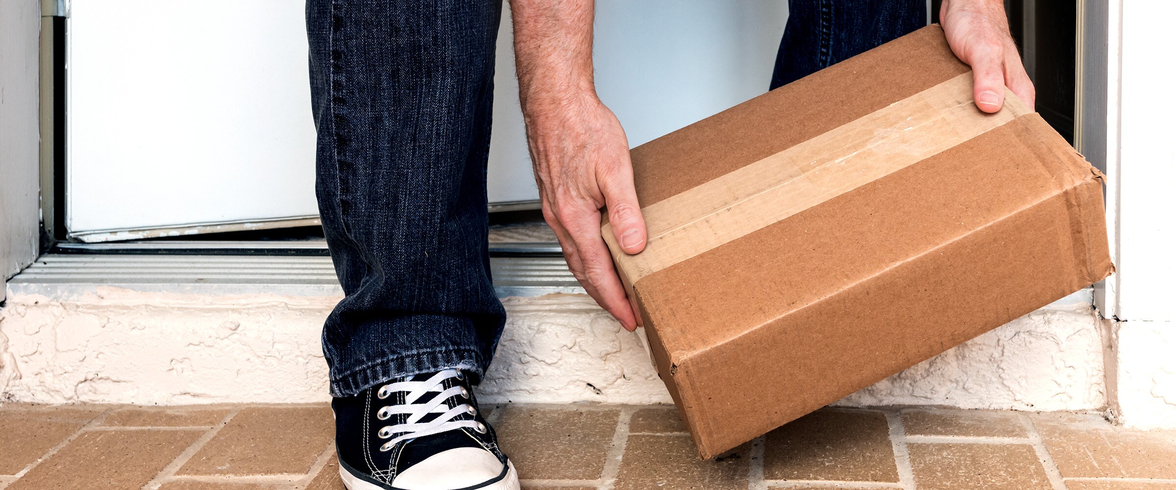 Photo of hands picking up a package at a doorstep.