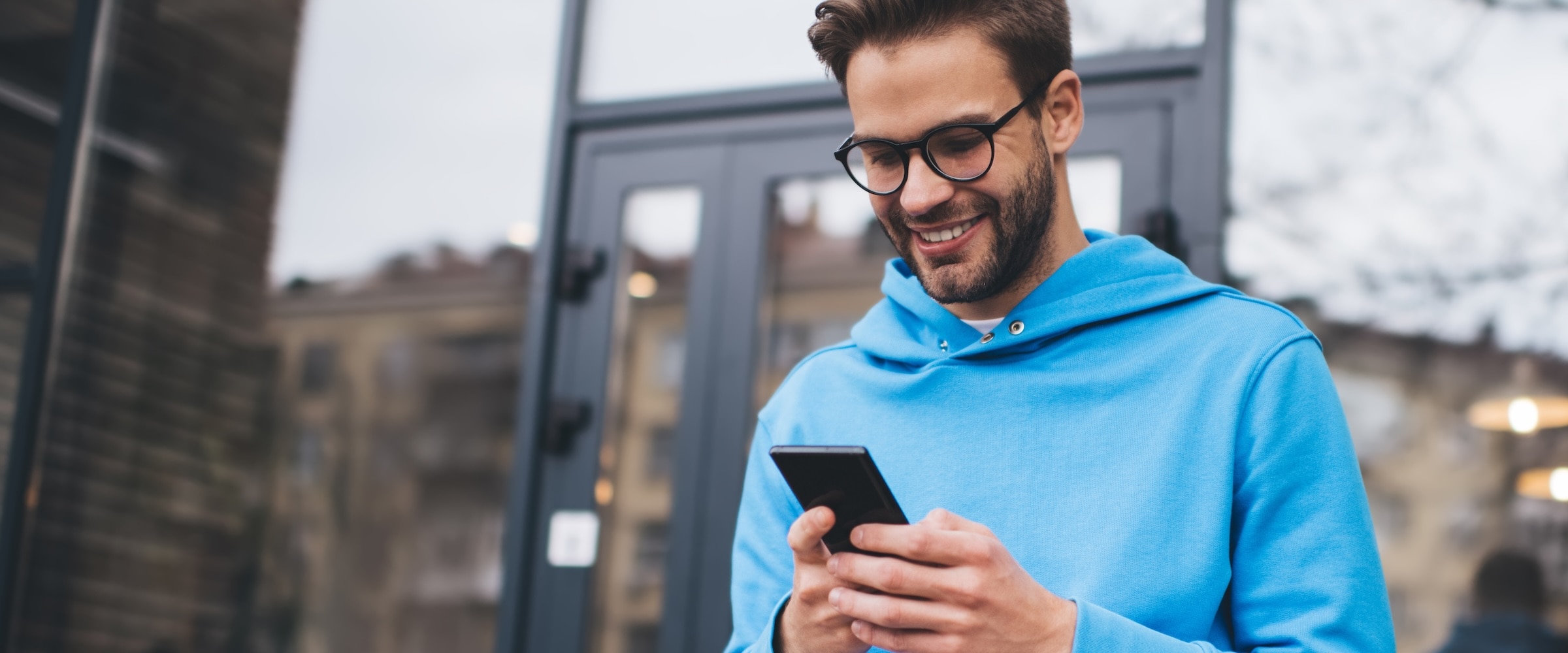 Photo of man outside store and looking at data on his smartphone.