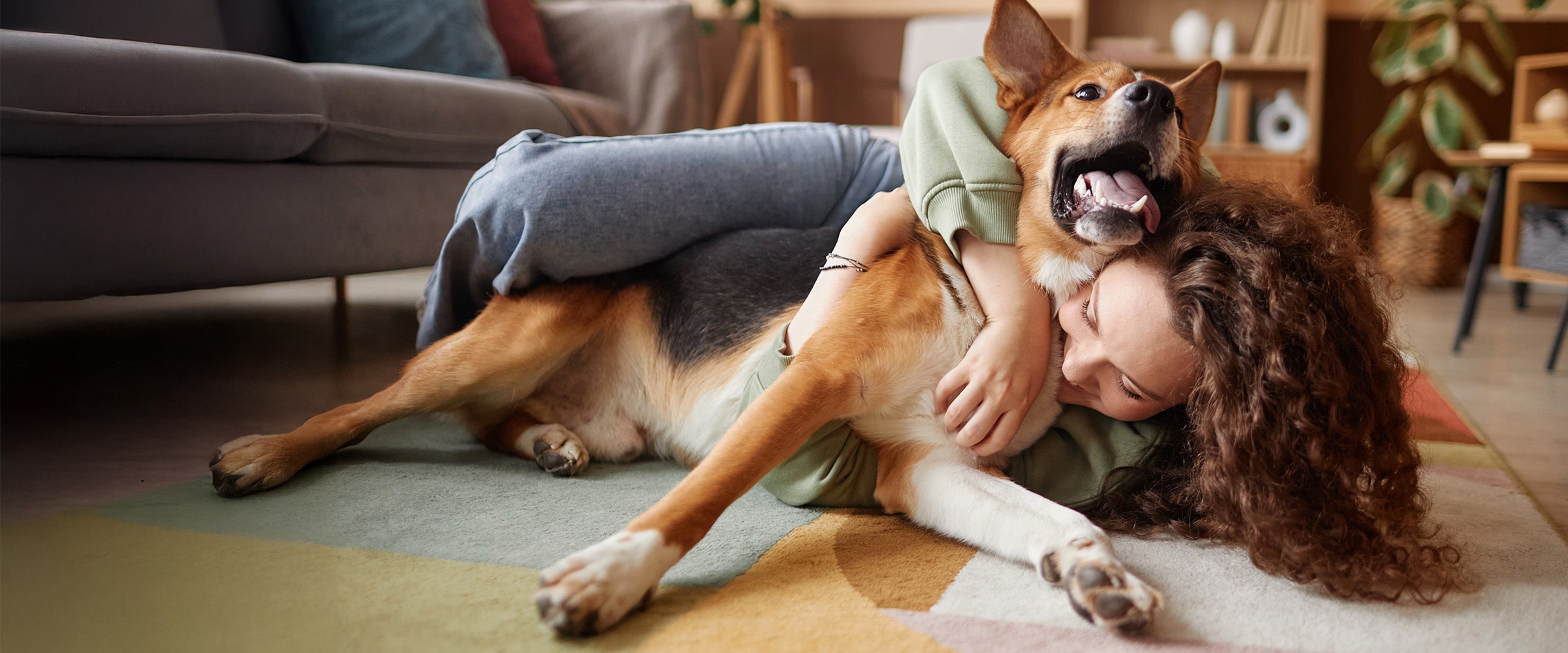 Photo of a woman playfully rolling on the floor with a dog.