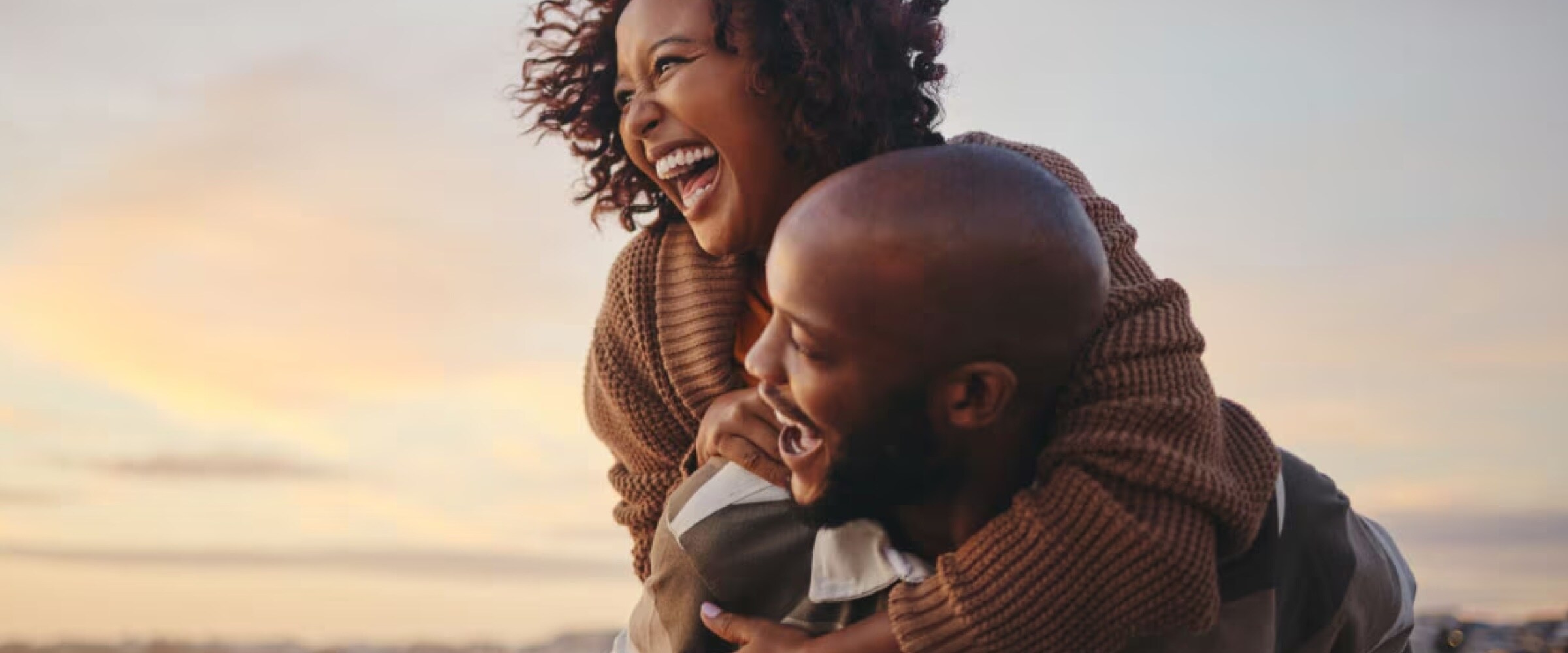 Photo of African American couple embracing in front of a sunset.