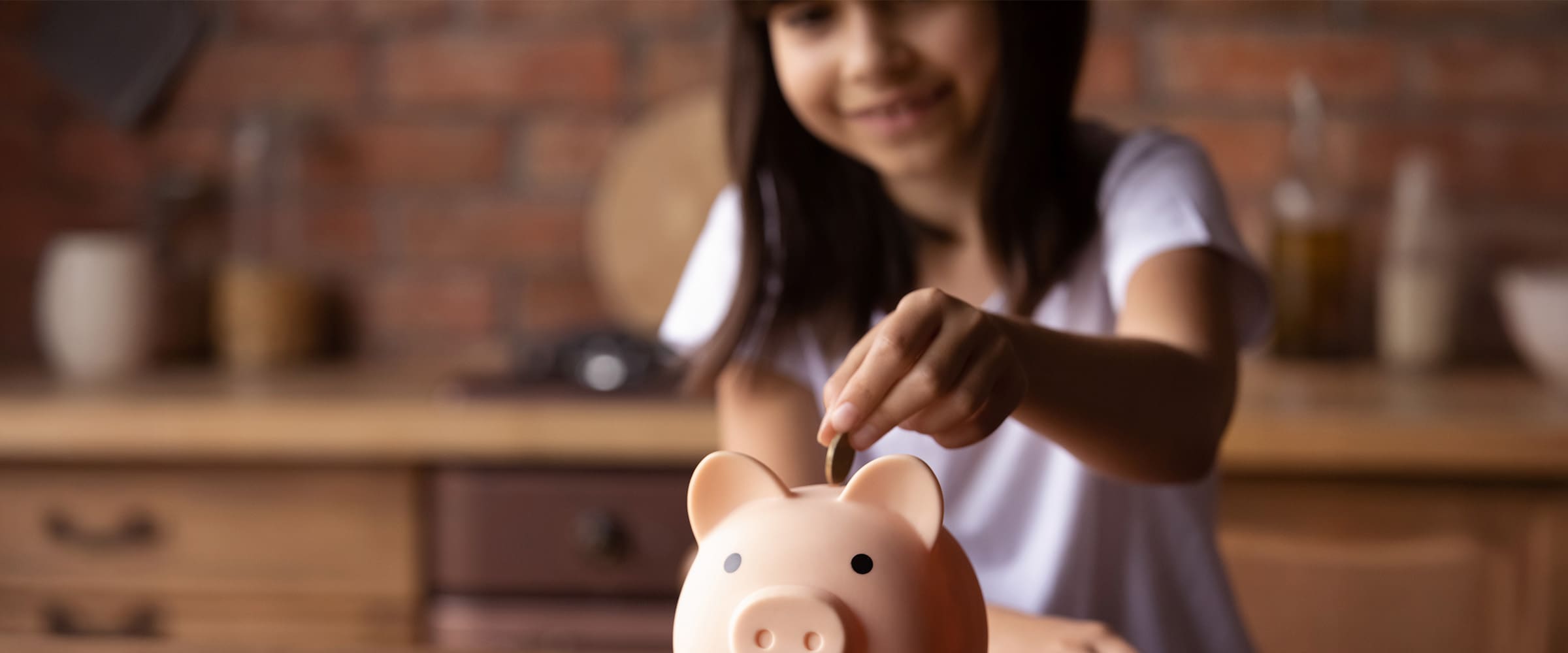 Photo of young girl putting a coin into a pink piggy bank.
