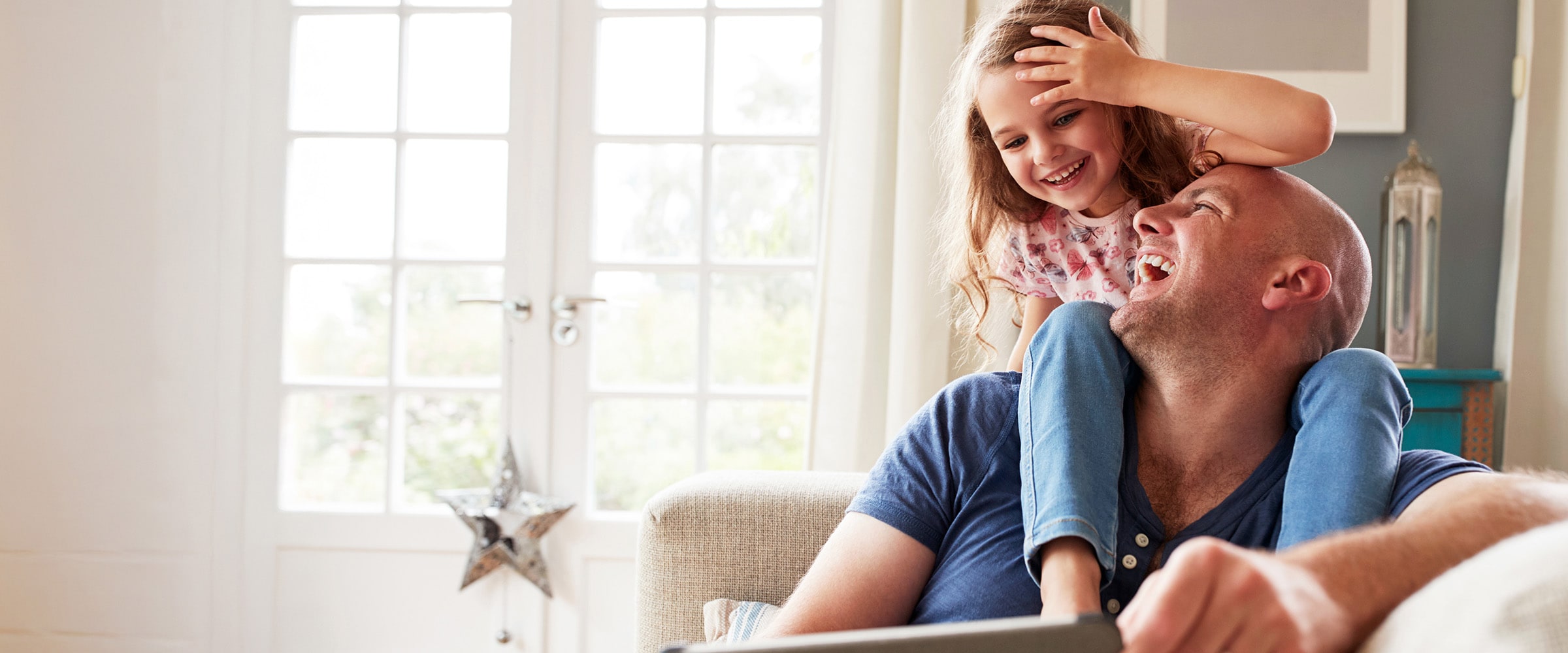 Photo of dad and daughter on the couch reading off a digital tablet.