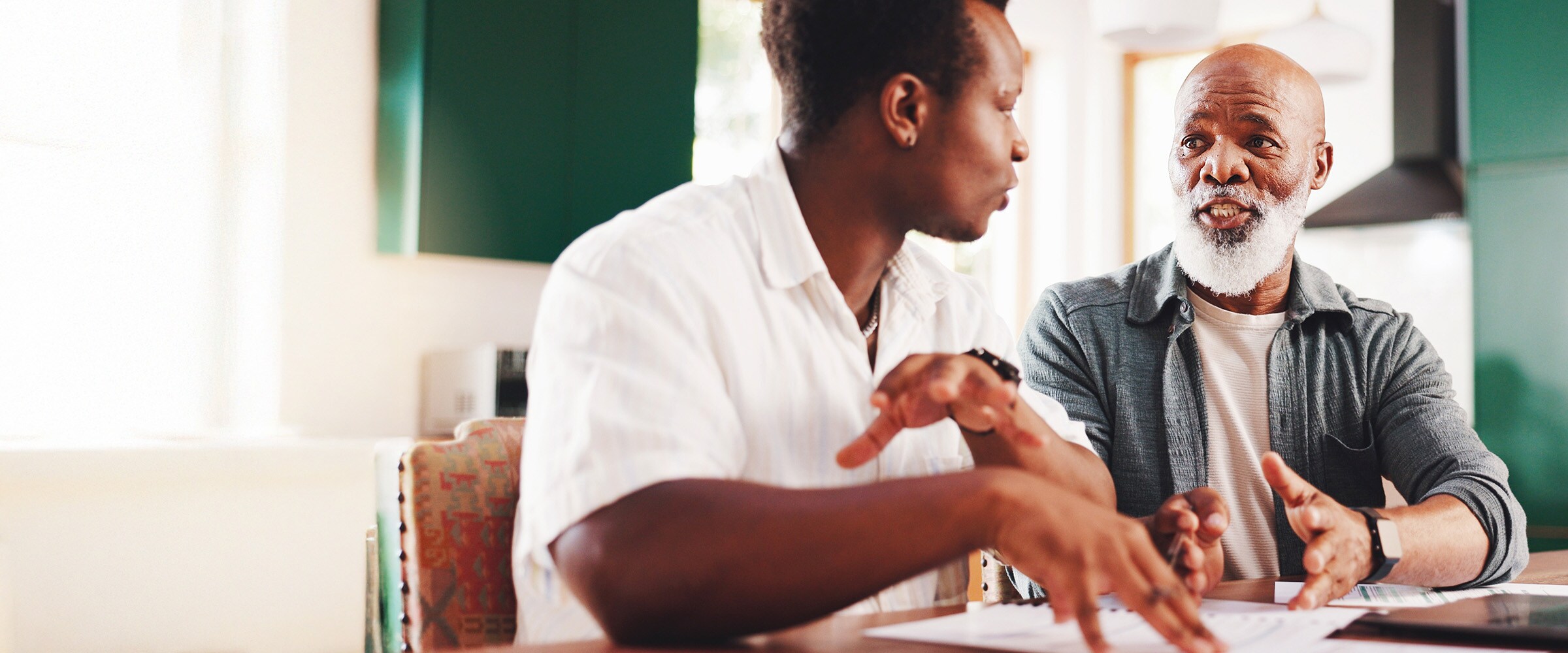 Photo of son talking to elderly African-american dad at the kitchen table.