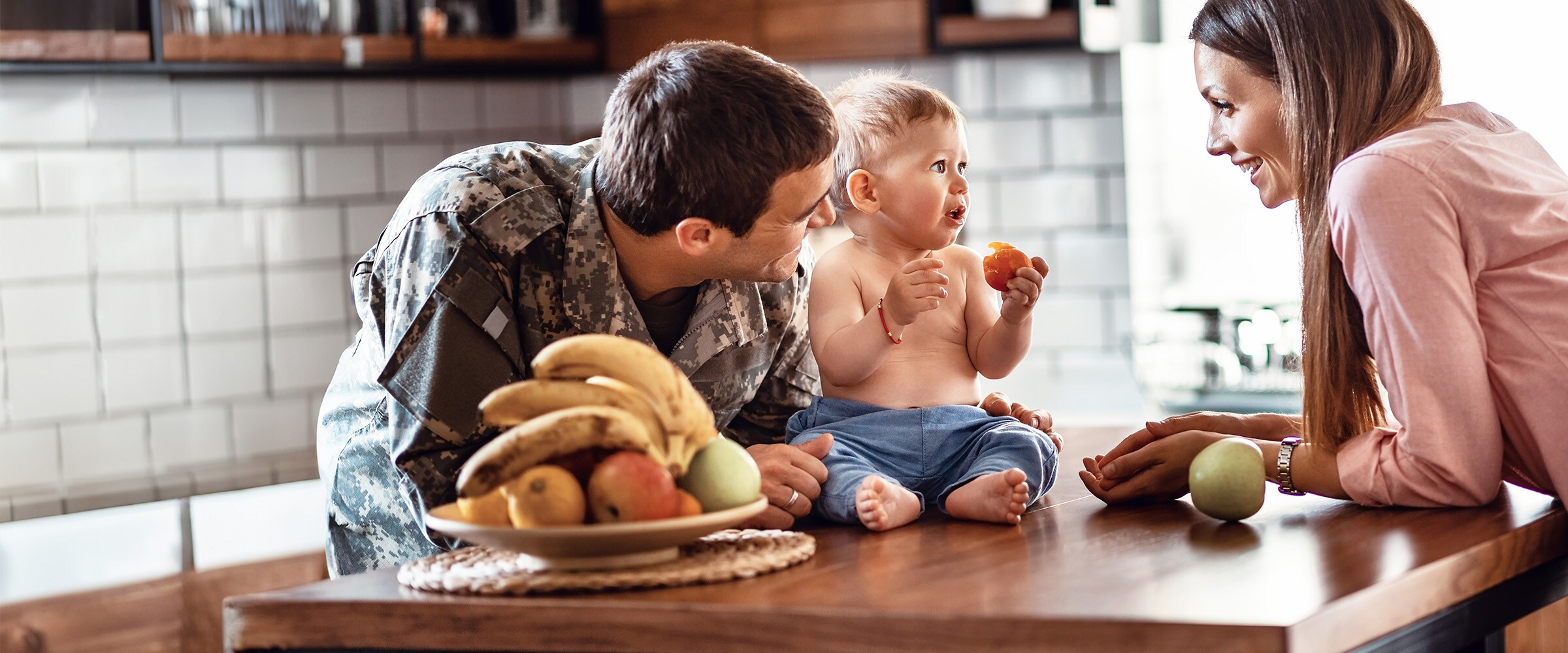Photo of mom and dad in military camo with young daughter at kitchen table.