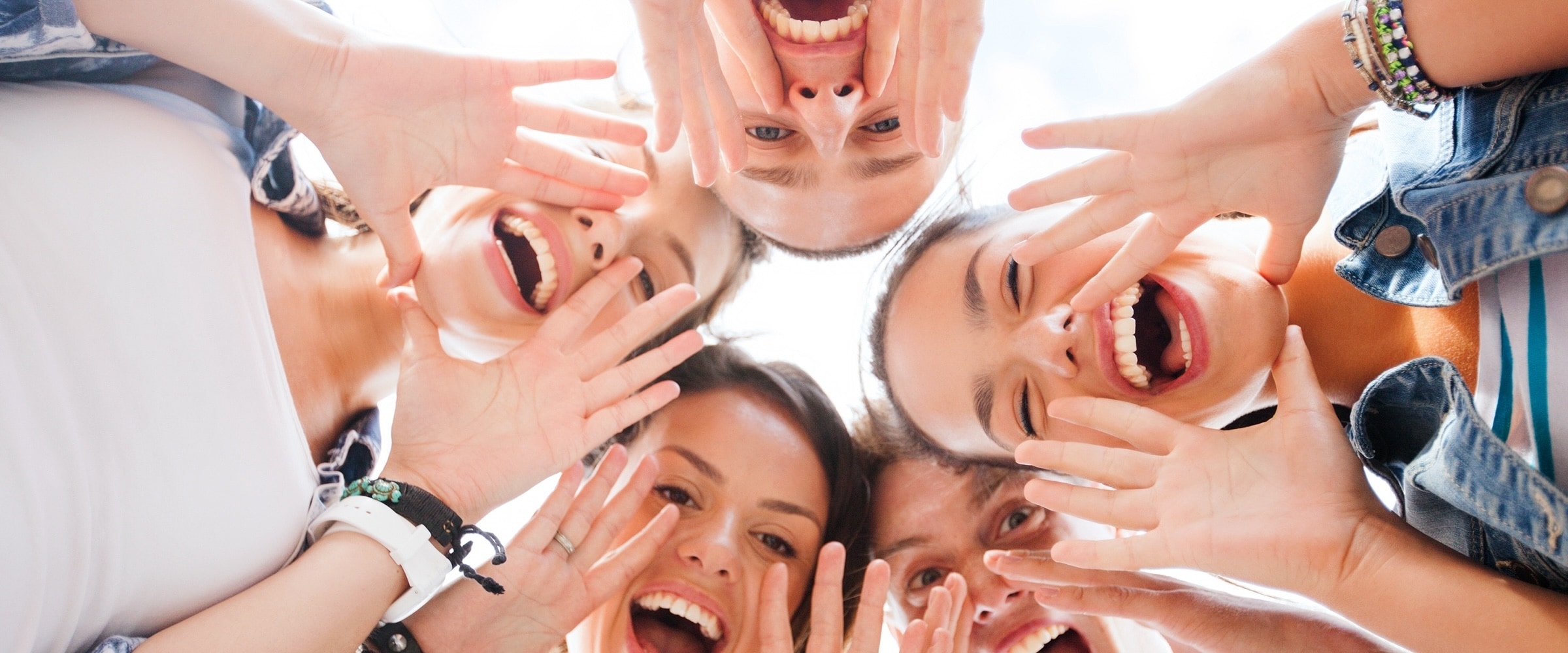 Photo looking up to a circle of young people shouting with mouths wide open.