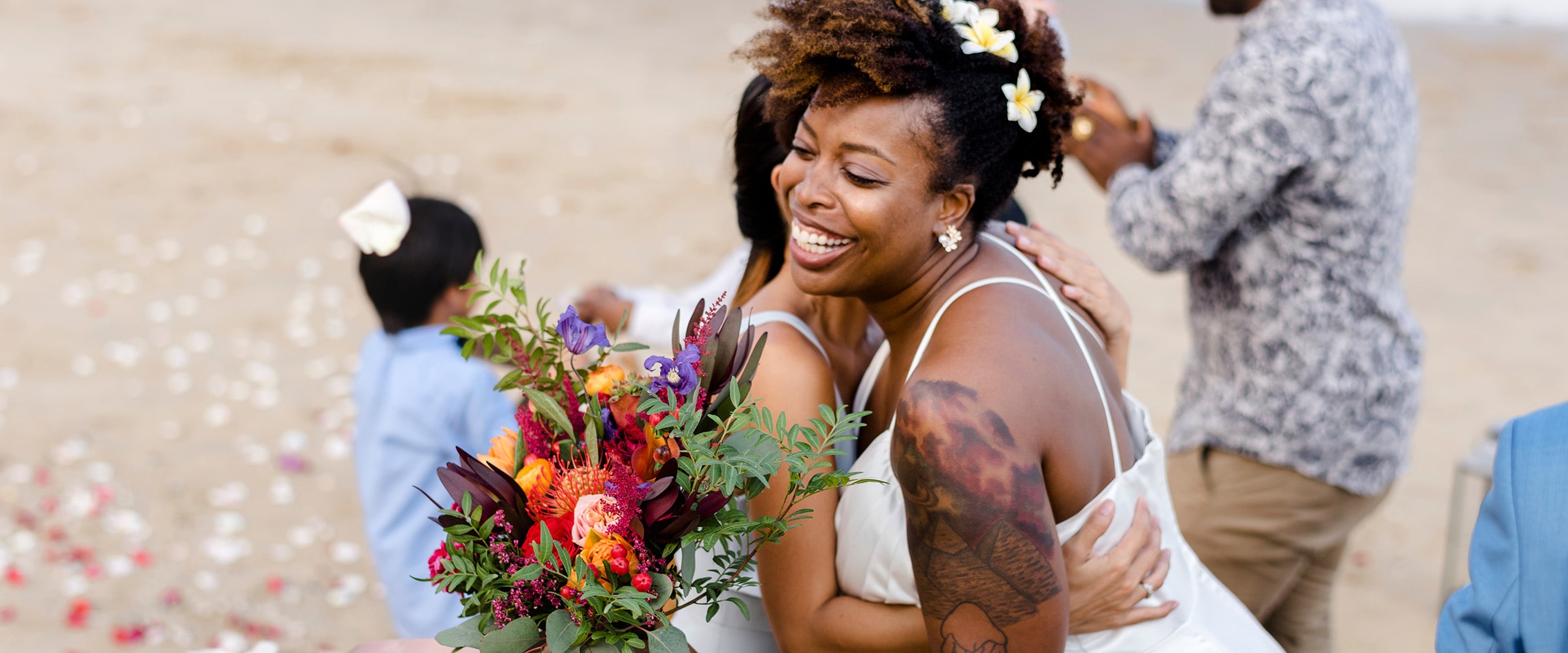Photo of bride and wedding guest embracing on the beach.