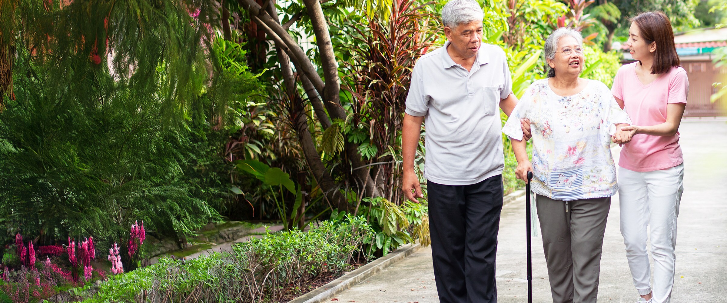 Photo of couple daughter walking with elderly couple down an outside path.