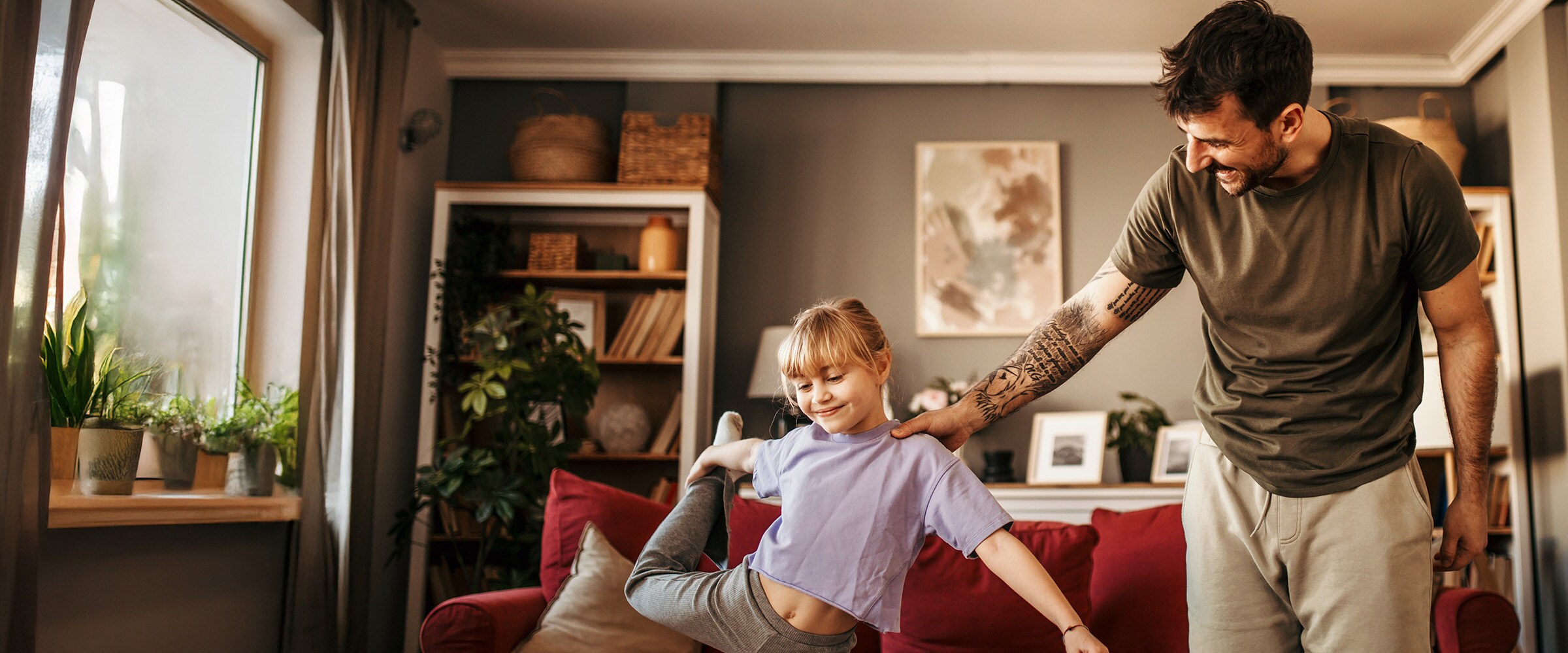 Photo of dad steadying smaller younger daughter who is balancing on one leg.