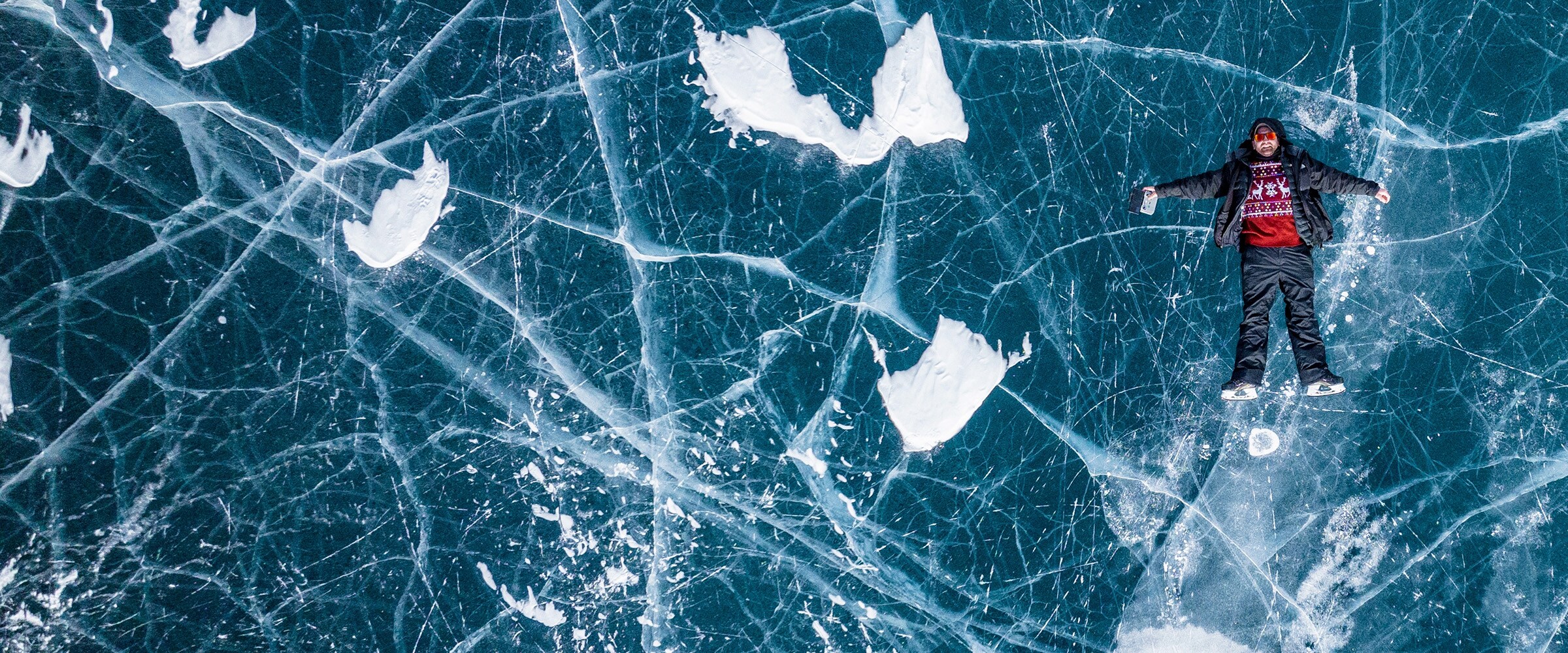 Photo of man on his back back on the deep blue ice of a frozen river.