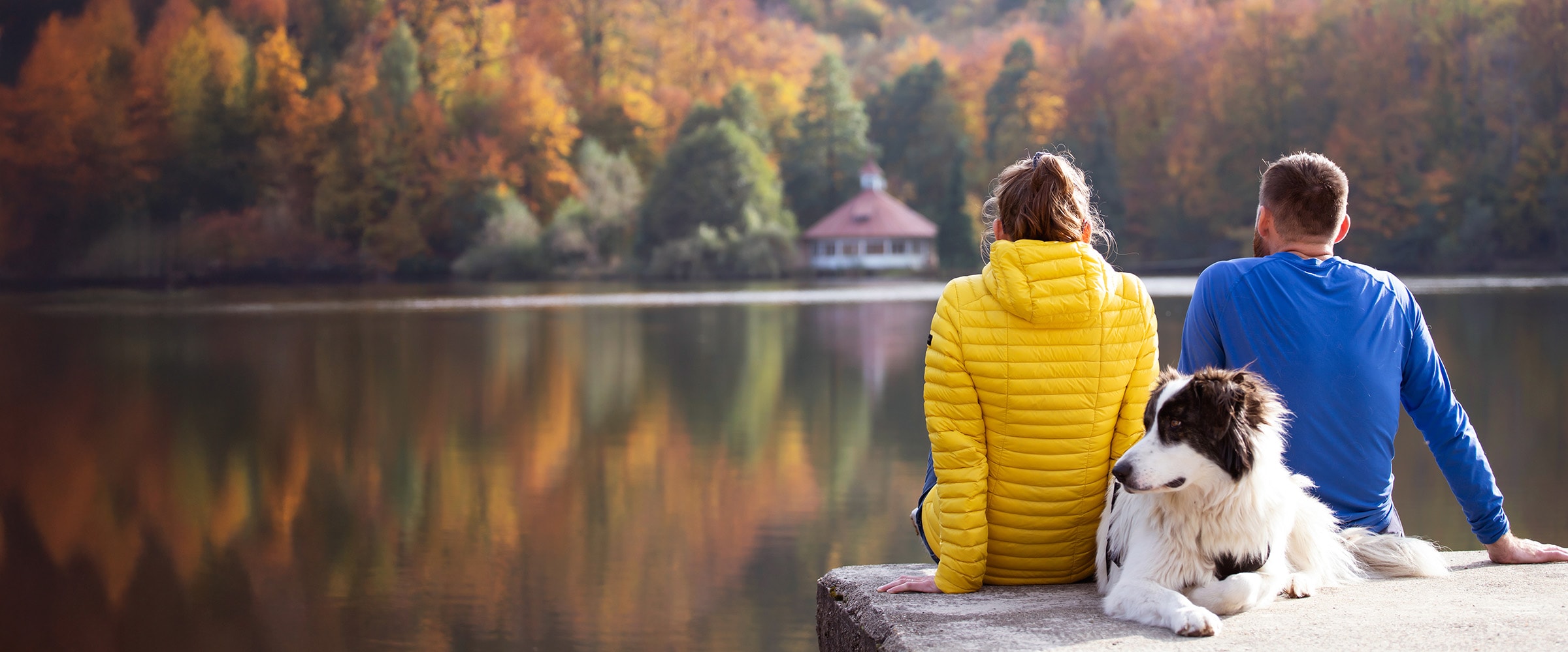 Photo of young couple in bright jackets sitting at the edge of a river.