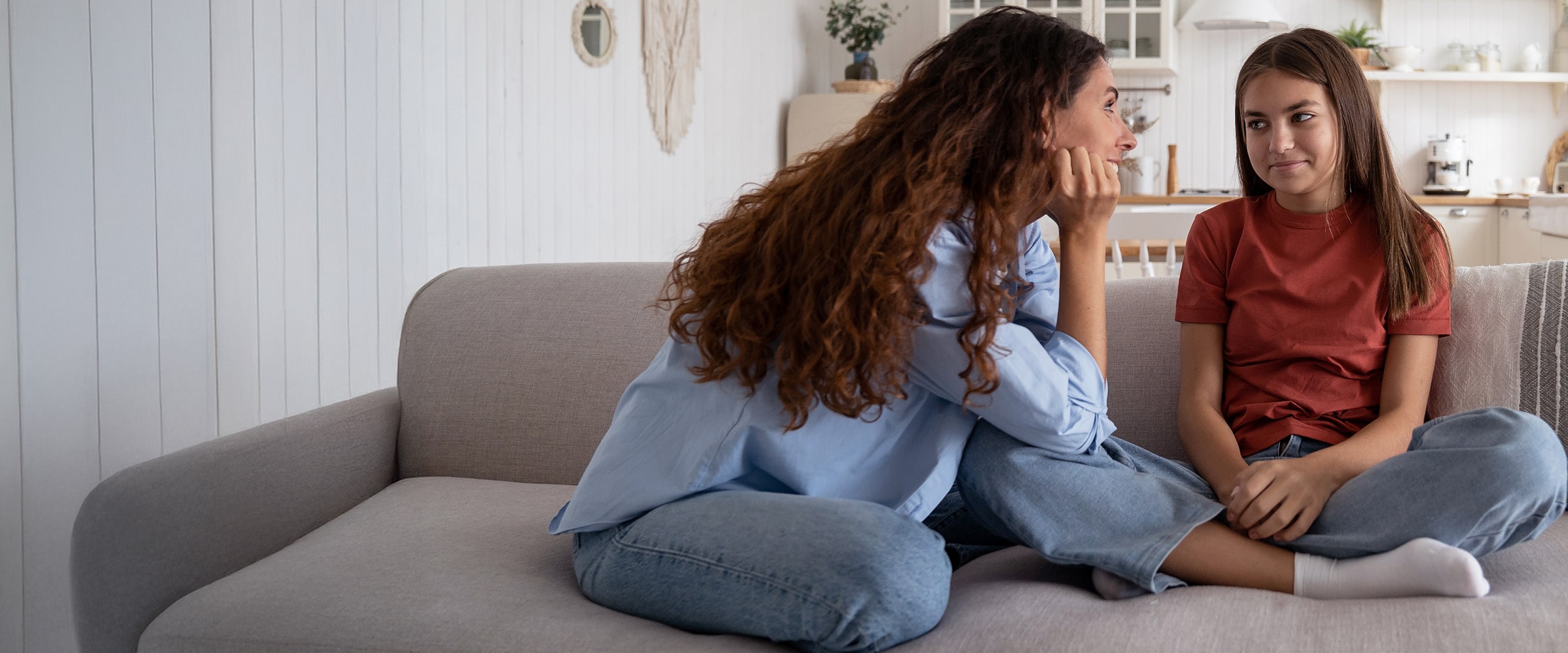Photo of woman and daughter sitting indian style on a sofa talking.