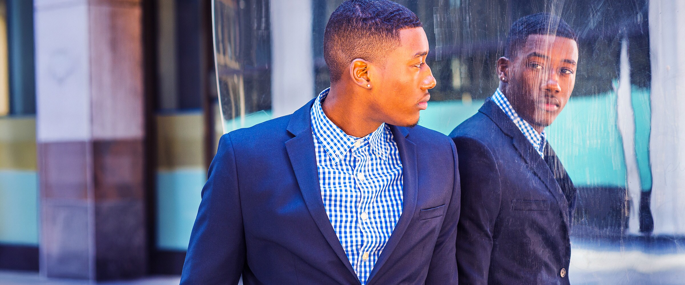 Photo of young adult looking at himself staring back in a building window.