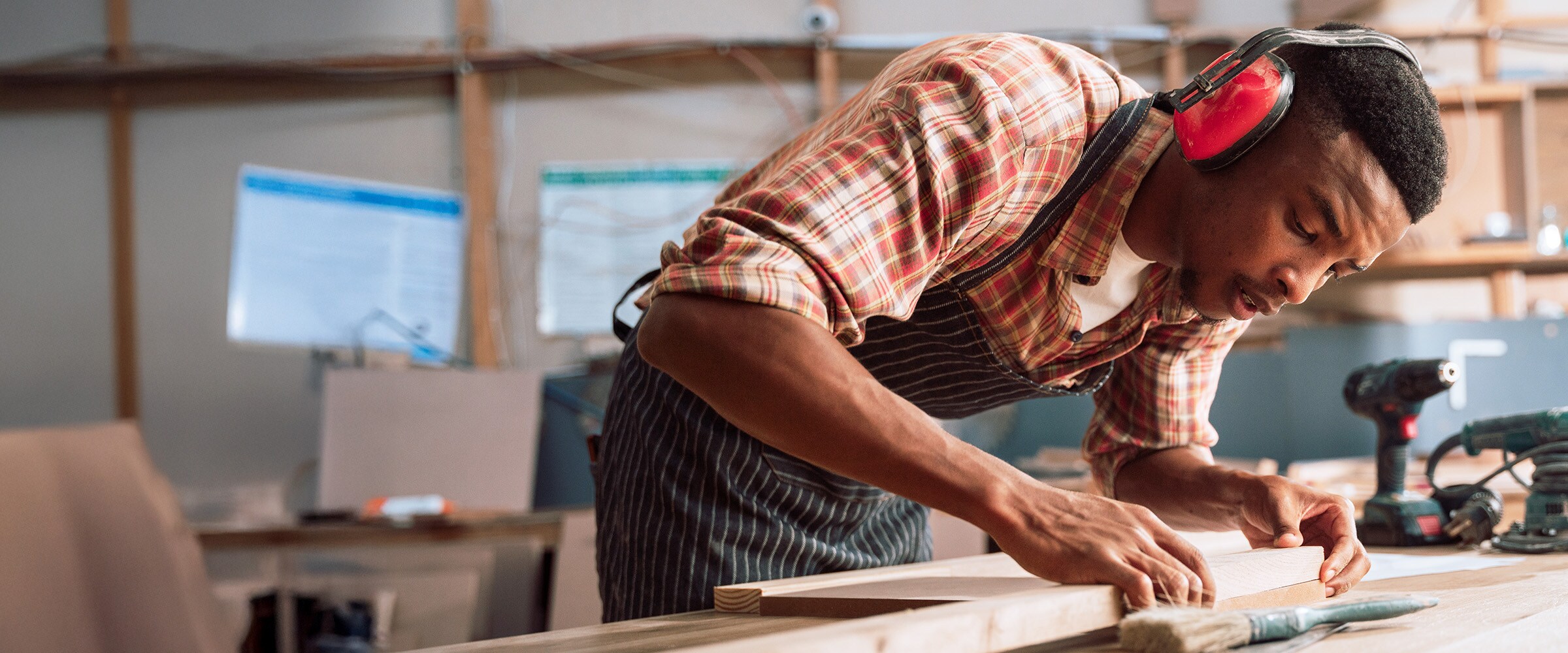 Photo of African-american man with headphones on working in a wood shop.
