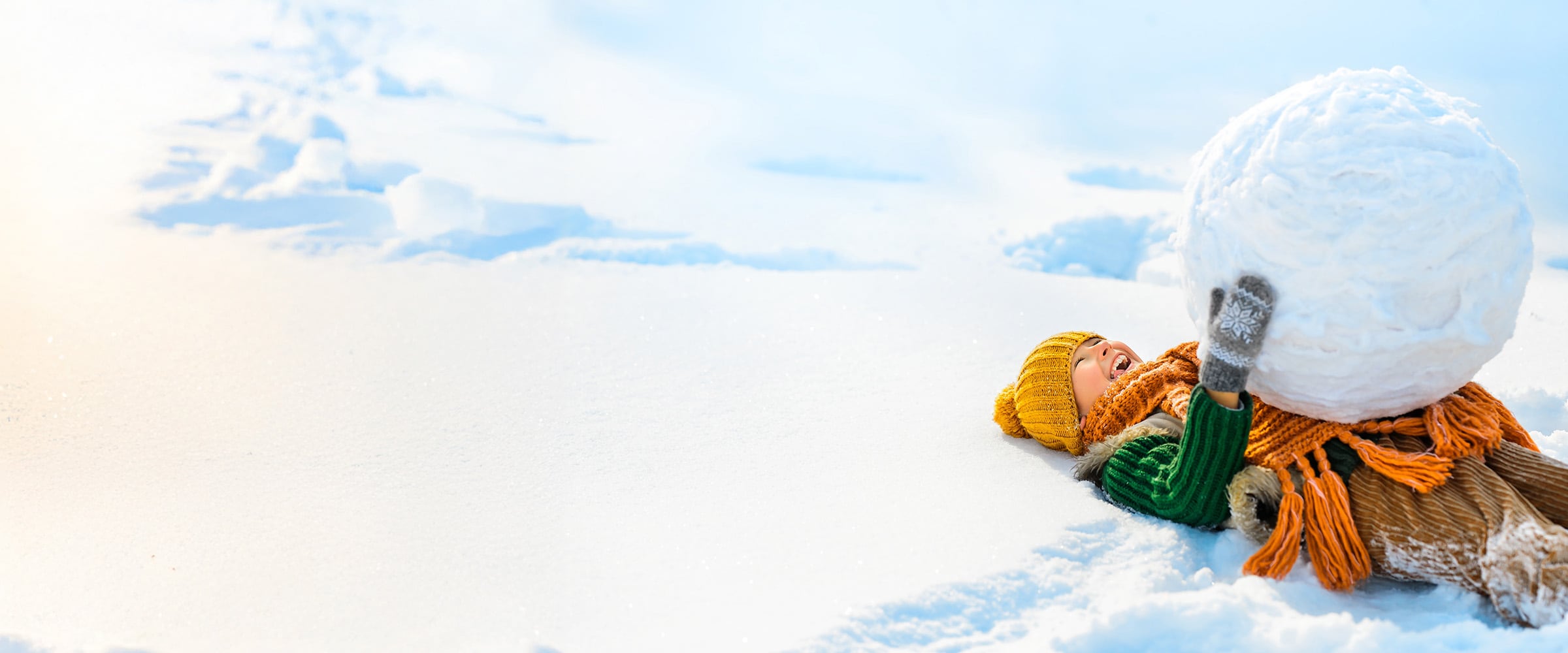 Photo of child in snow gear holding a giant snowball.