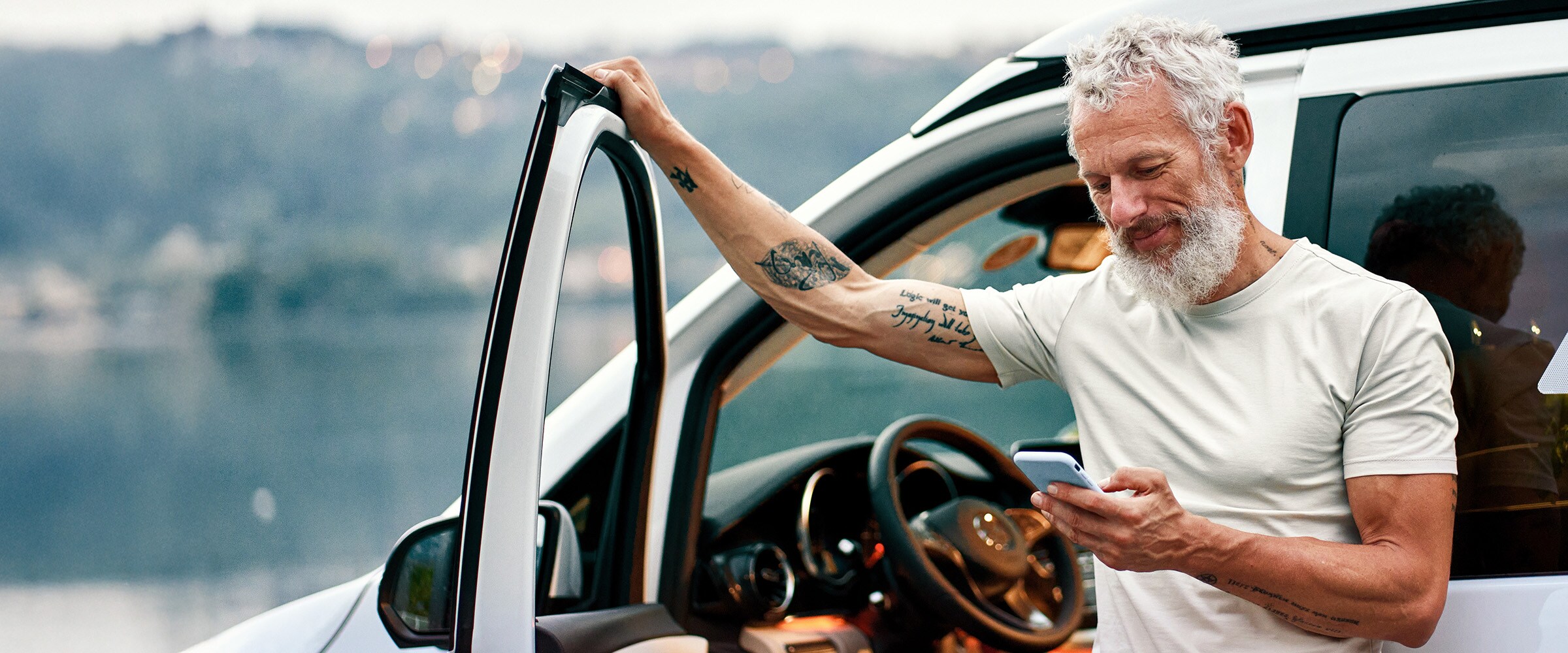 Photo of a older man standing outside of his car and looking at smartphone.