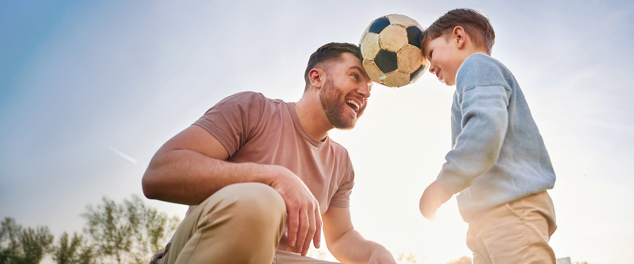 Photo of dad and son holding up a soccer ball between their foreheads.