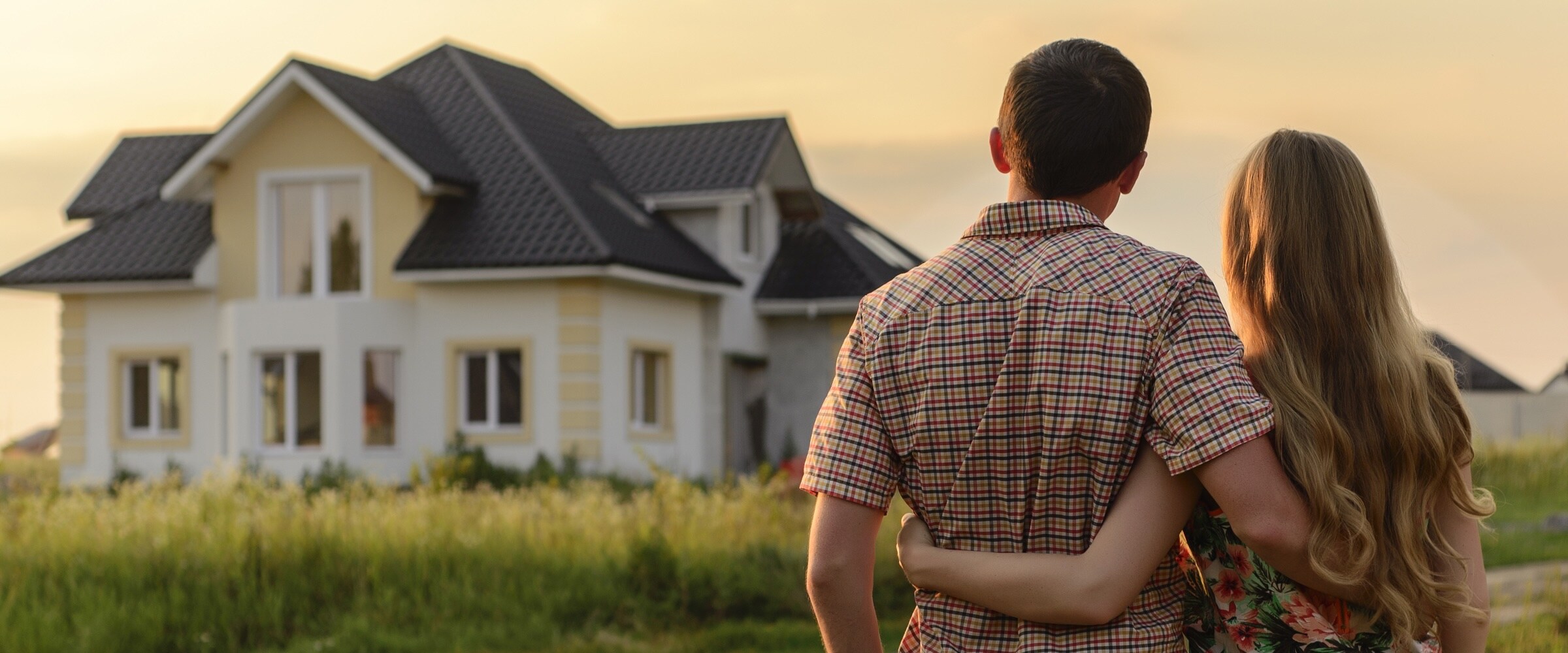 Photo of a young couple embracing as they look at their new home.