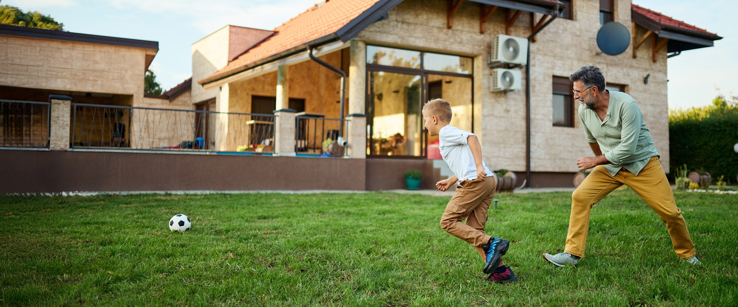 Photo of dad and son playing soccer in front of a home.