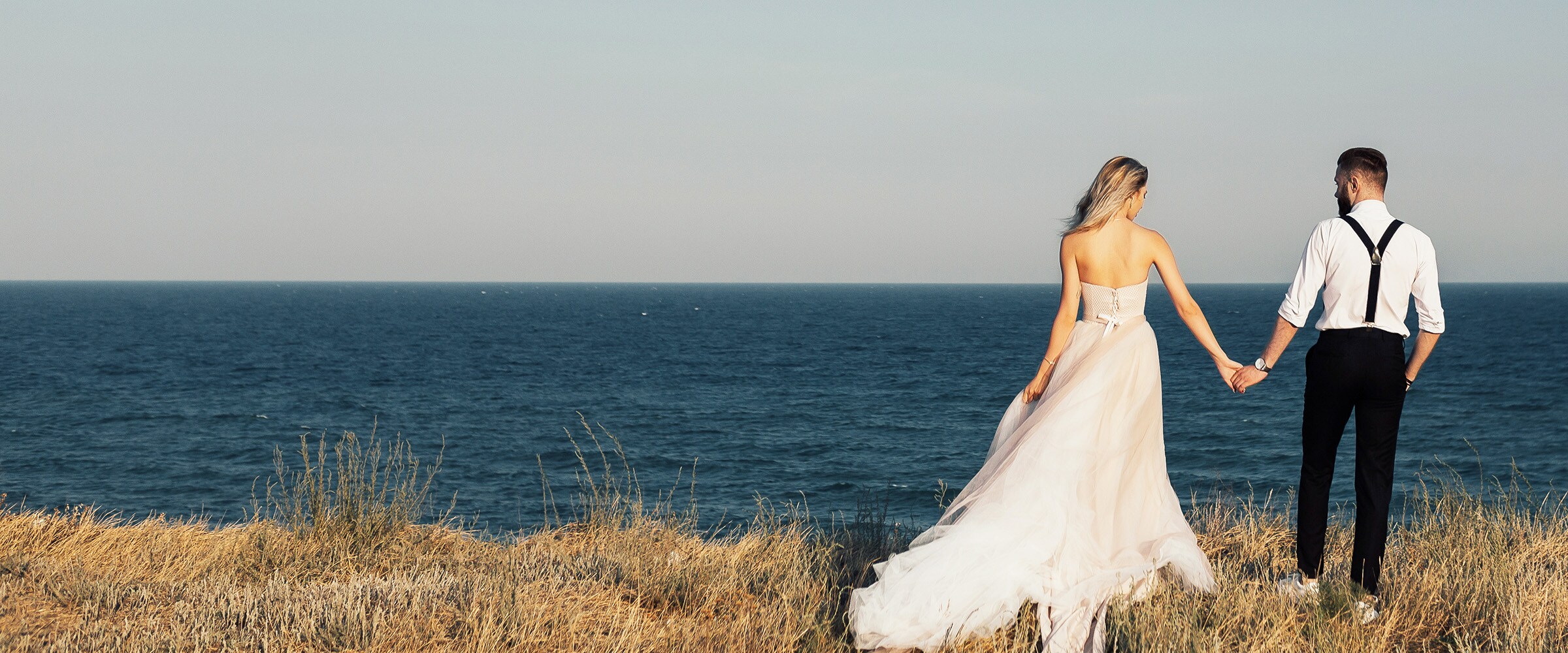 Photo of woman in bridal gown and groom walking near a beach shore.