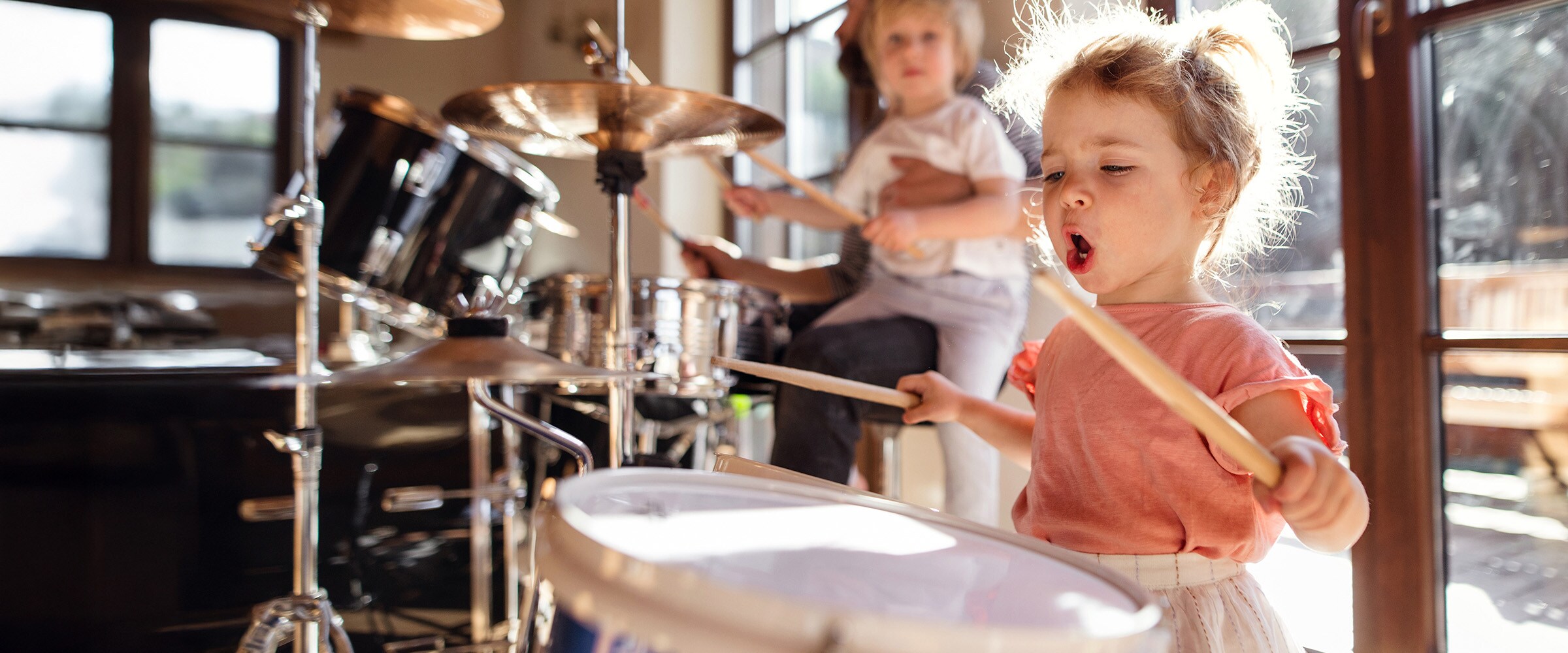 Photo of toddler with drumsticks pounding a drum.