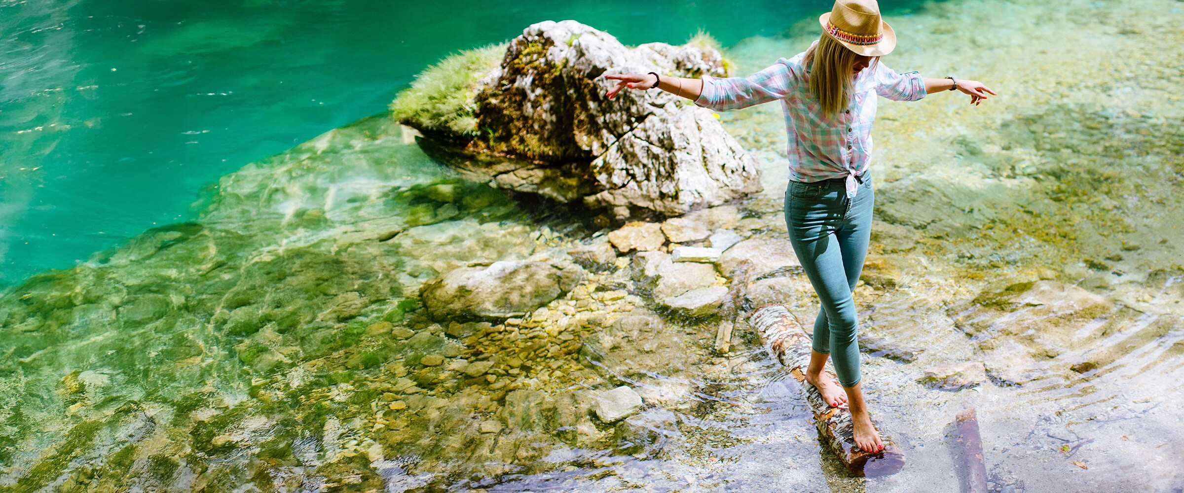 Photo of woman balancing on large tree branch at the river's edge.