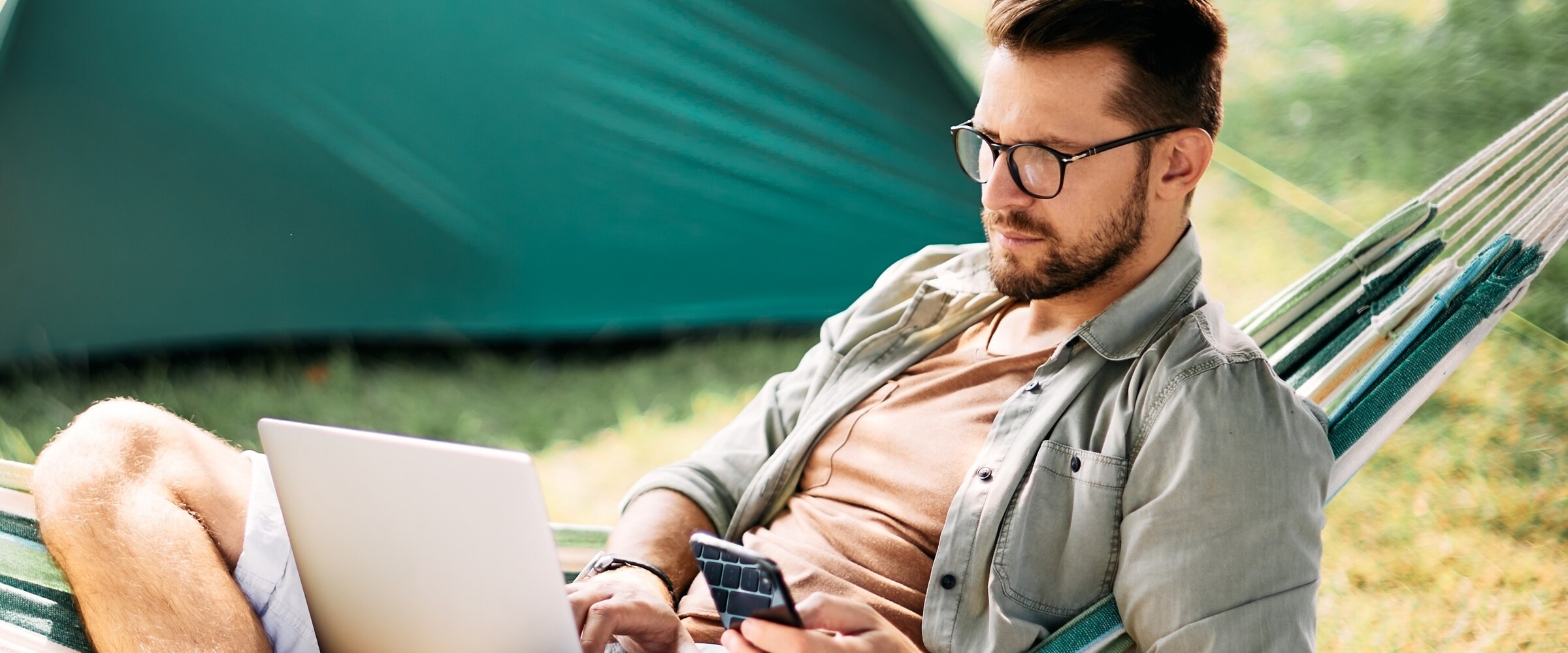 Photo of man with glasses sitting on hammock looking at his smartphone.