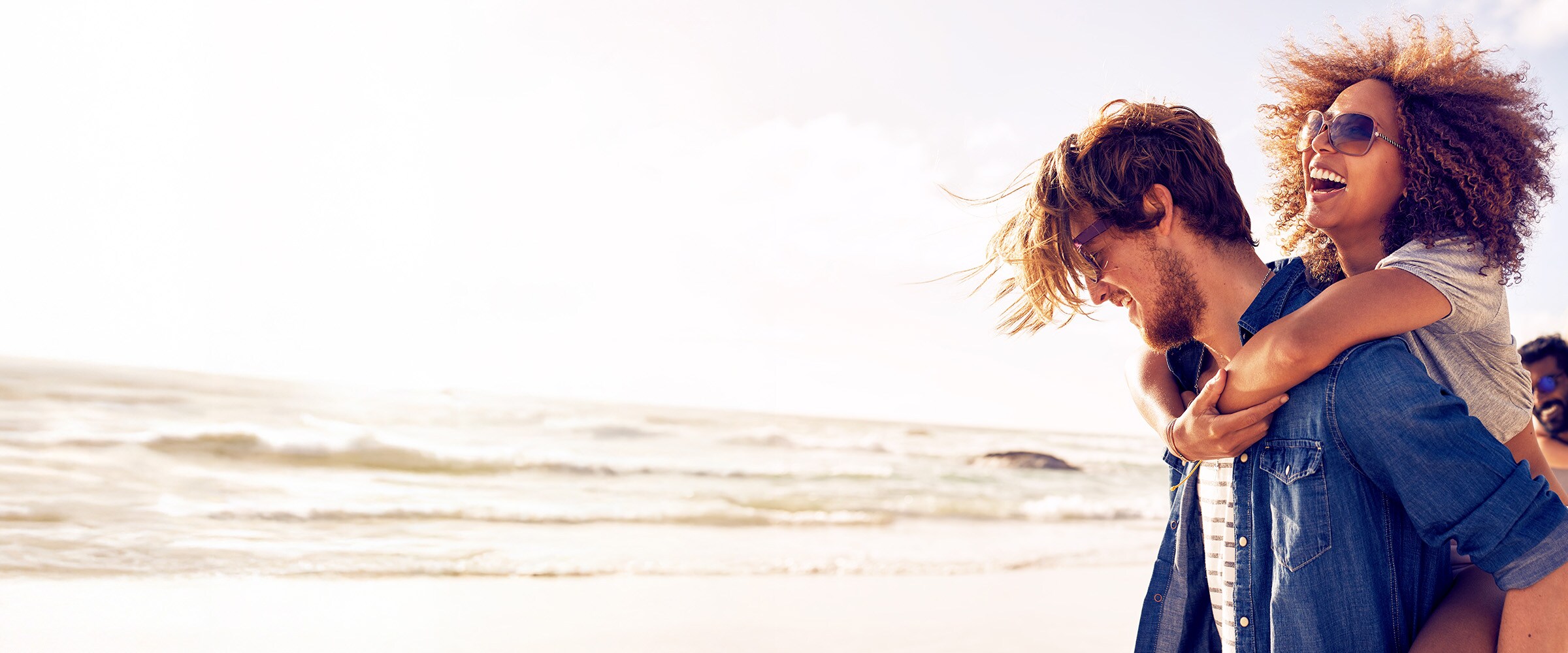 Image of couple. Women is riding on man's back at the beach.