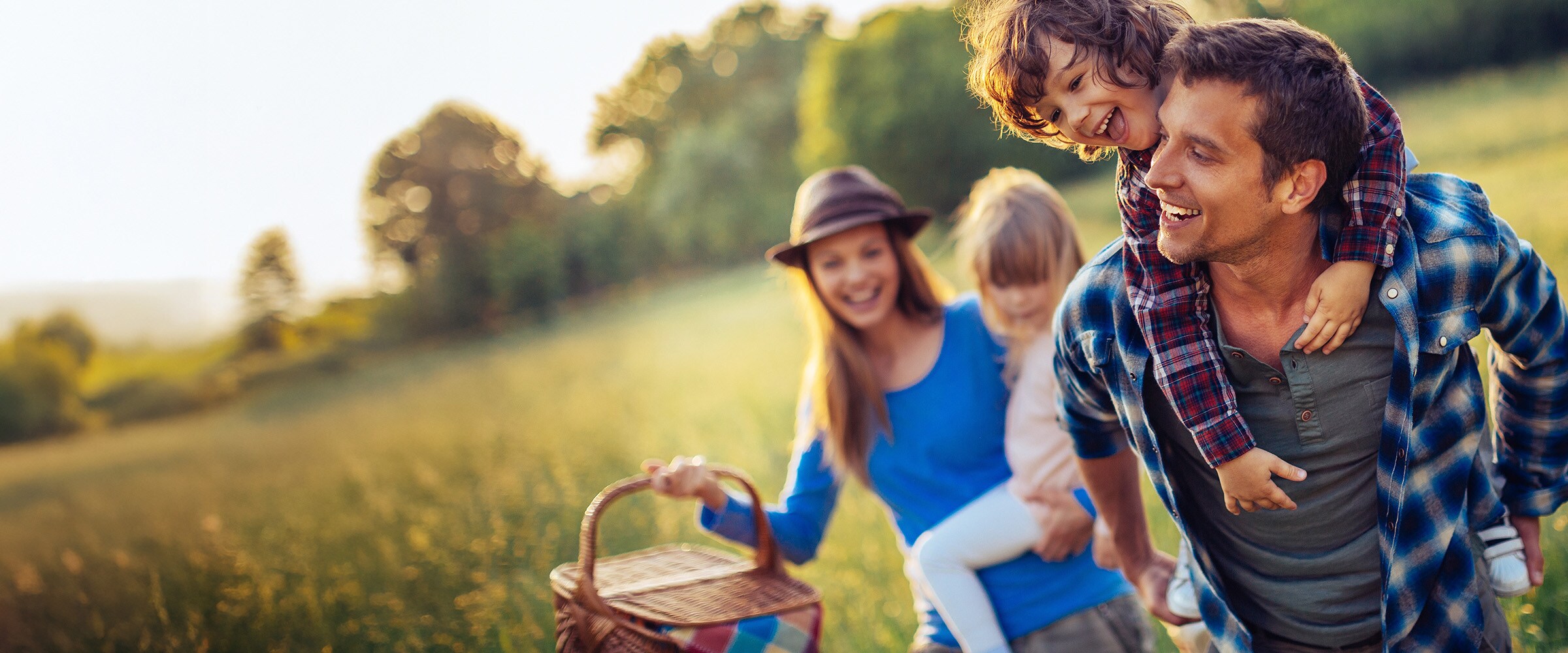 Photo of young family walking in field with a picnic basket.