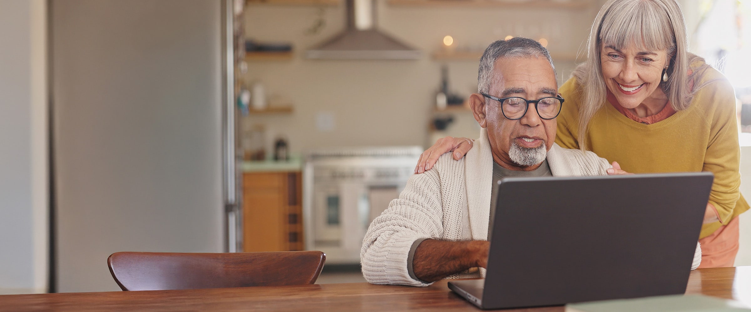Photo of older couple looking at their laptop at the kitchen table.
