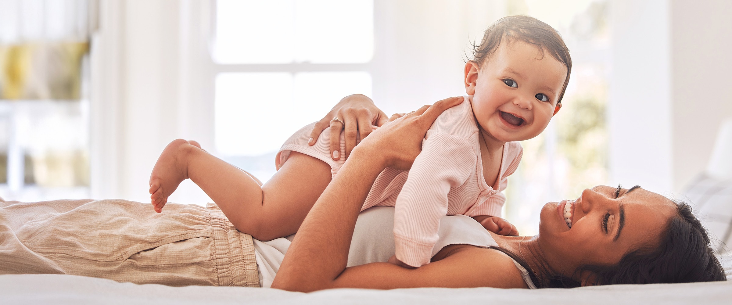 Photo of woman lying on bed and holding up her baby above her.