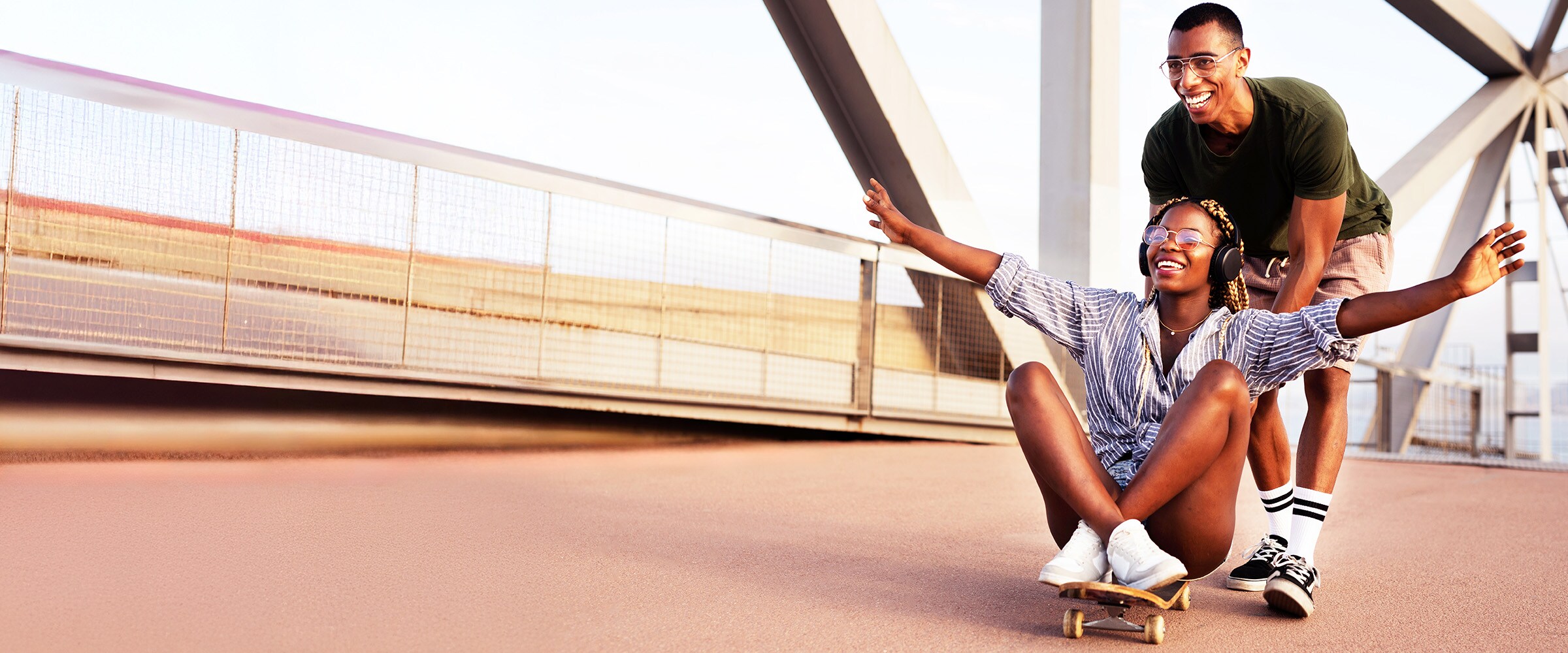 Photo of woman laughing as she is being pushed on a skateboard by a man.