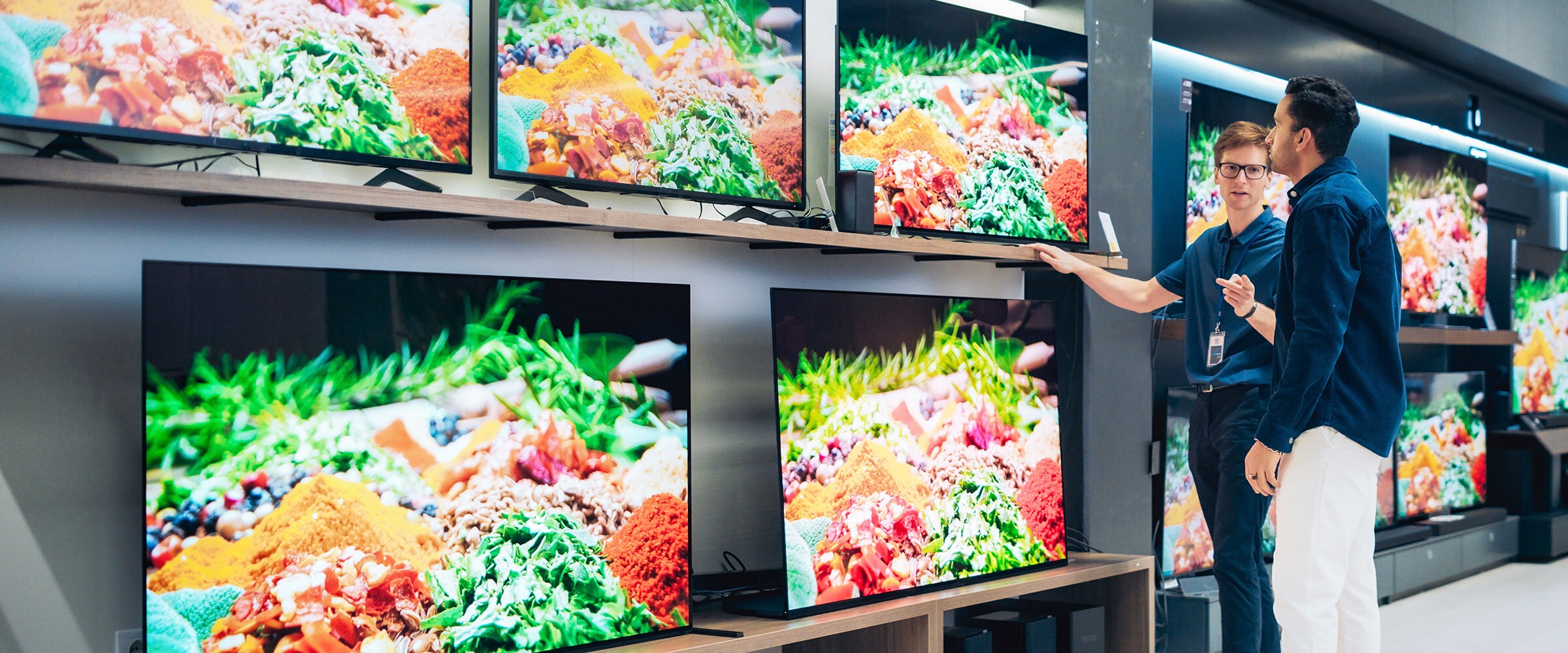 Photo of man looking at high definition TVs lined up at a store.