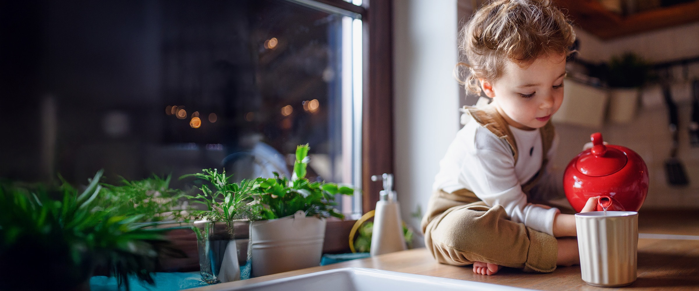 Photo of a child pouring water from a red teapot into a cup.