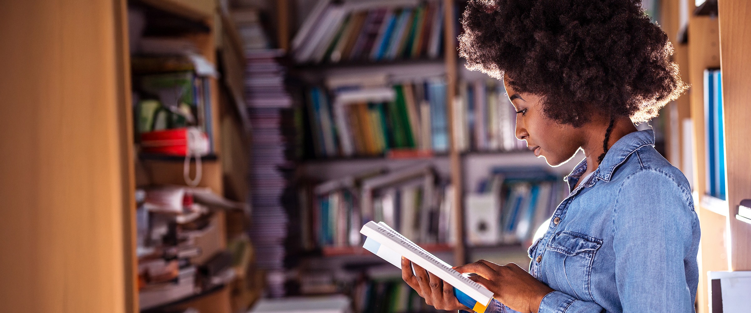 Photo of African American woman looking at a book in a library.