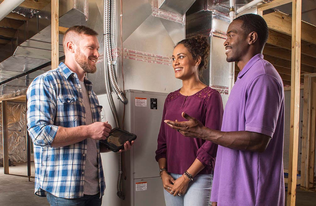 Couple and HVAC professional standing in unfinished basement discussing financing.