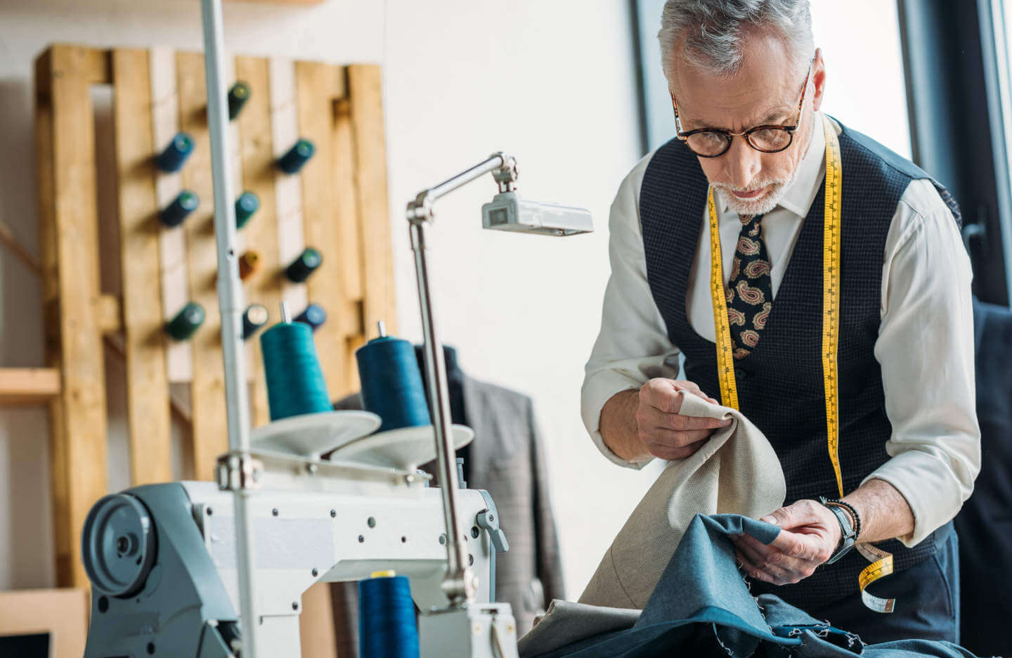 Tailor with tape measure around neck comparing fabrics