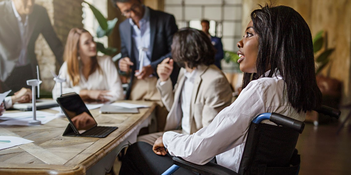 Photo of woman in wheelchair at lead desk in a business meeting.