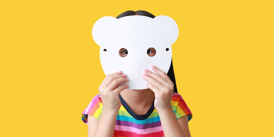 Photo of young child hiding her face behind a white mask.